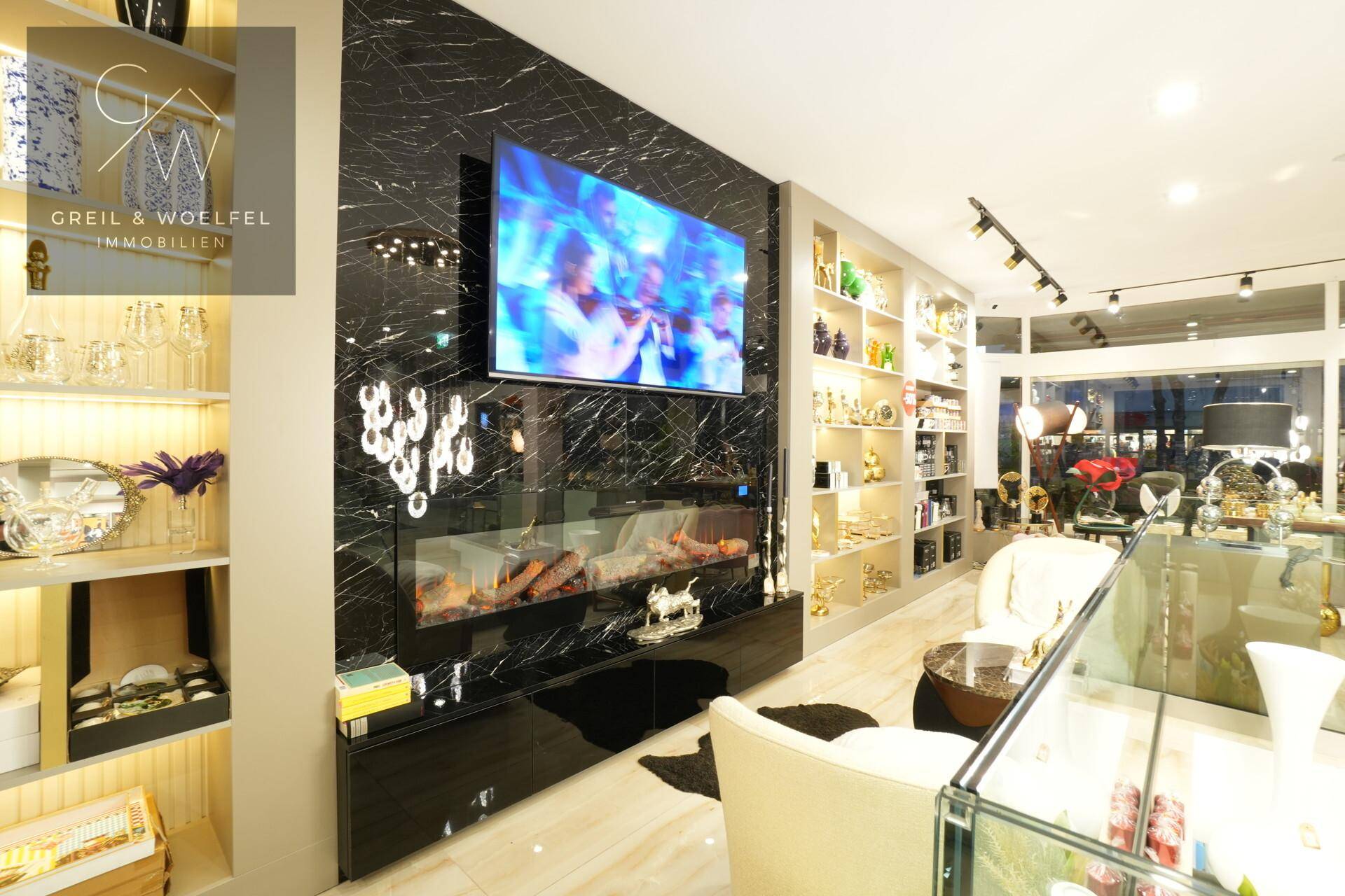 Moderner Verkaufsraum mit einer schwarzen Marmorwand, integriertem Fernseher und dekorativem Kamin.
