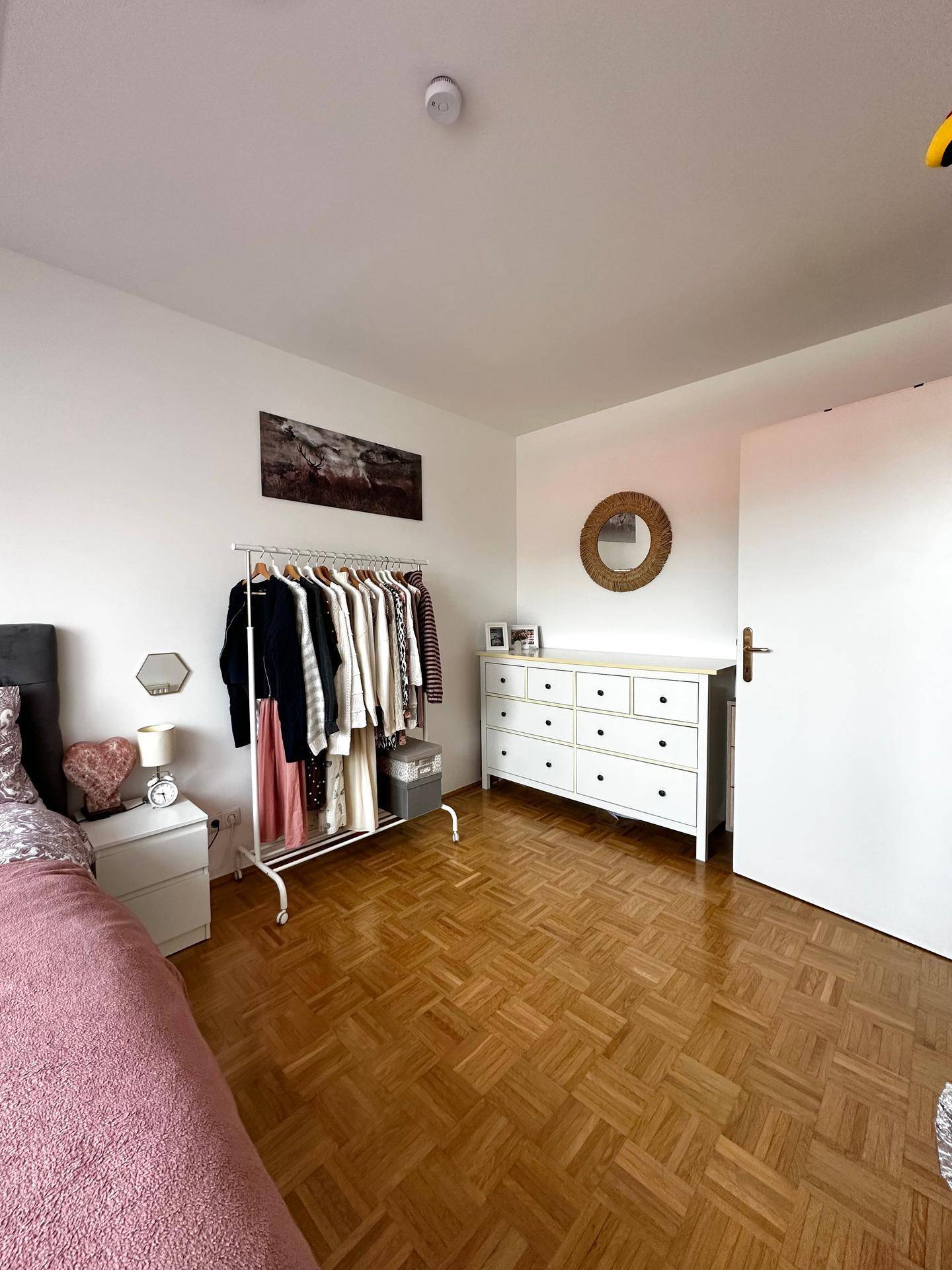 Schlafzimmer mit Parkettboden, Kleiderstange und einer weißen Kommode mit Schubladen.