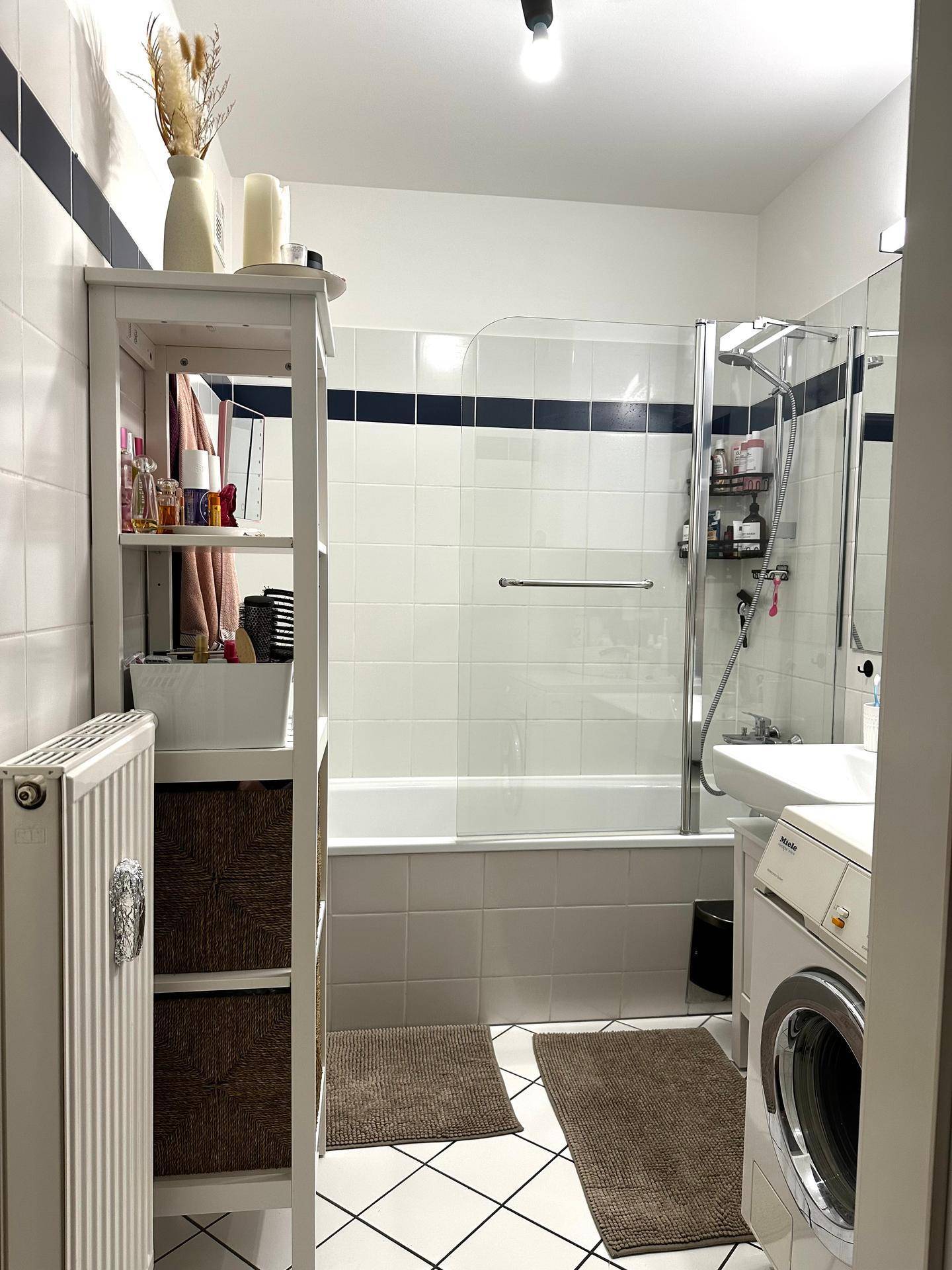 Badezimmer mit Badewanne, Duschabtrennung, Waschbecken und integrierter Waschmaschine.