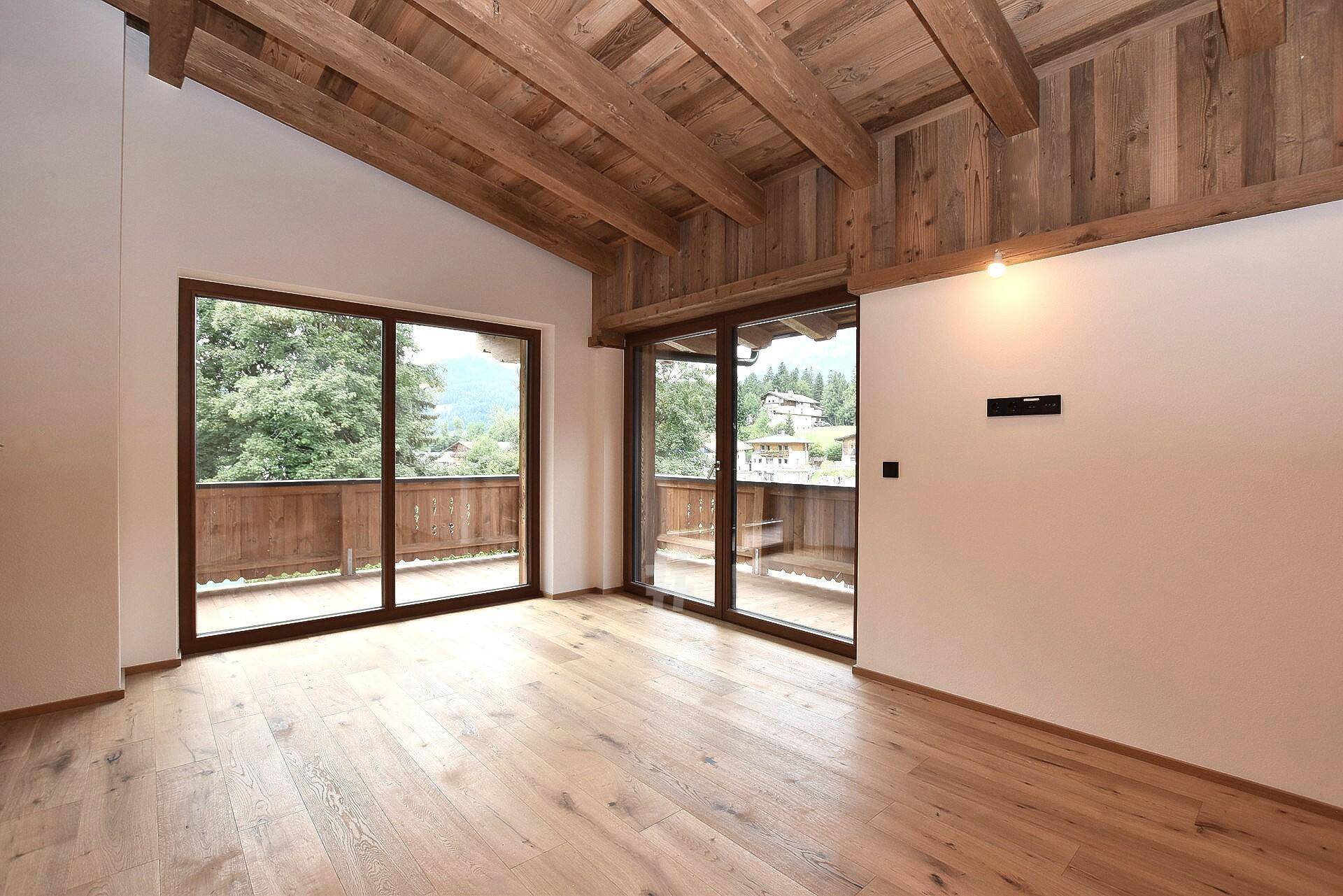 Heller Raum mit Holzboden, hoher Decke und Balkonzugang mit malerischem Bergblick.