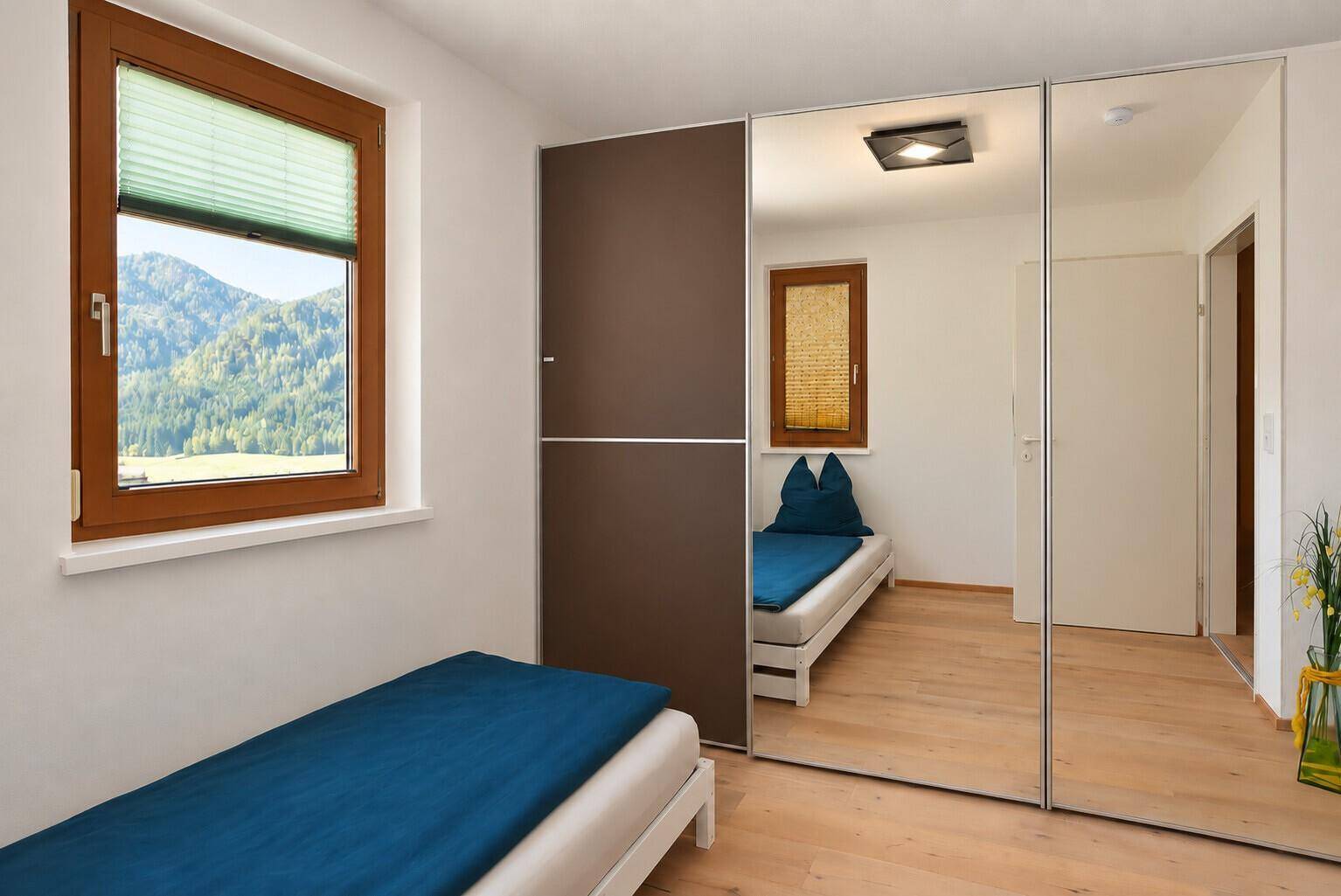 Schlafzimmer mit Einzelbett, Spiegelschrank und Fenster mit Blick ins Grüne.