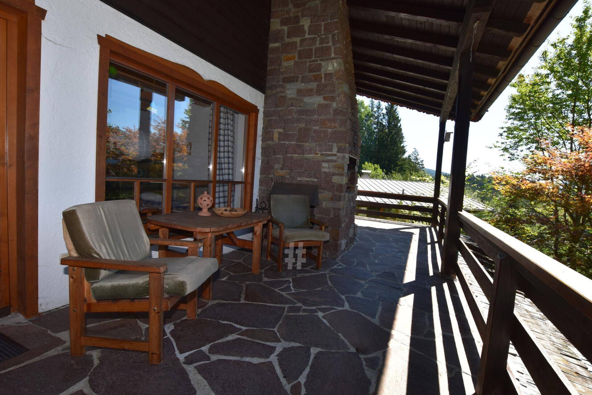 Überdachter Balkon mit Steinwandkamin und rustikalen Holzmöbeln, ideal für entspannte Stunden im Freien.