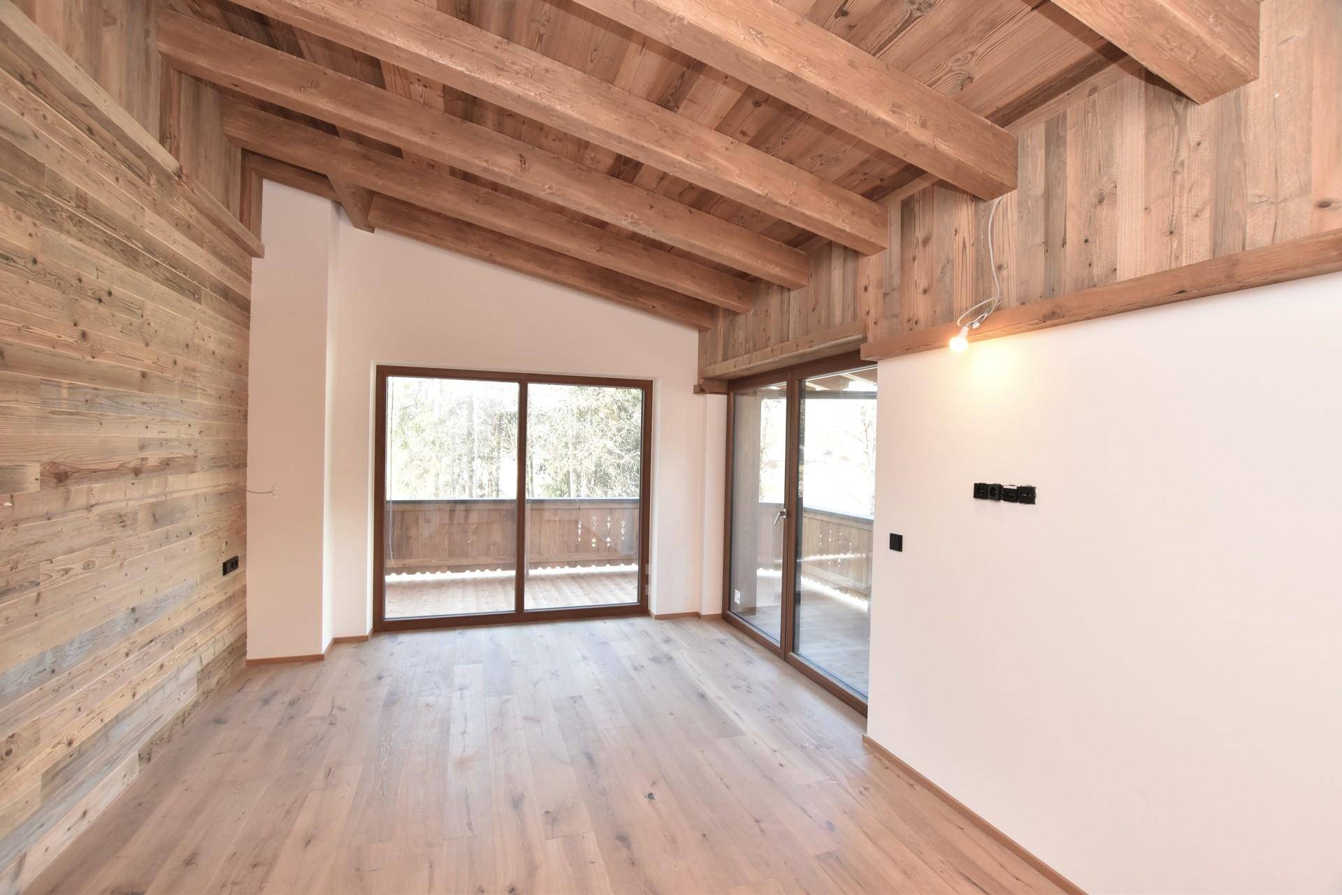 Heller Raum mit Holzboden, hoher Decke und Balkonzugang, umgeben von natürlicher Landschaft.