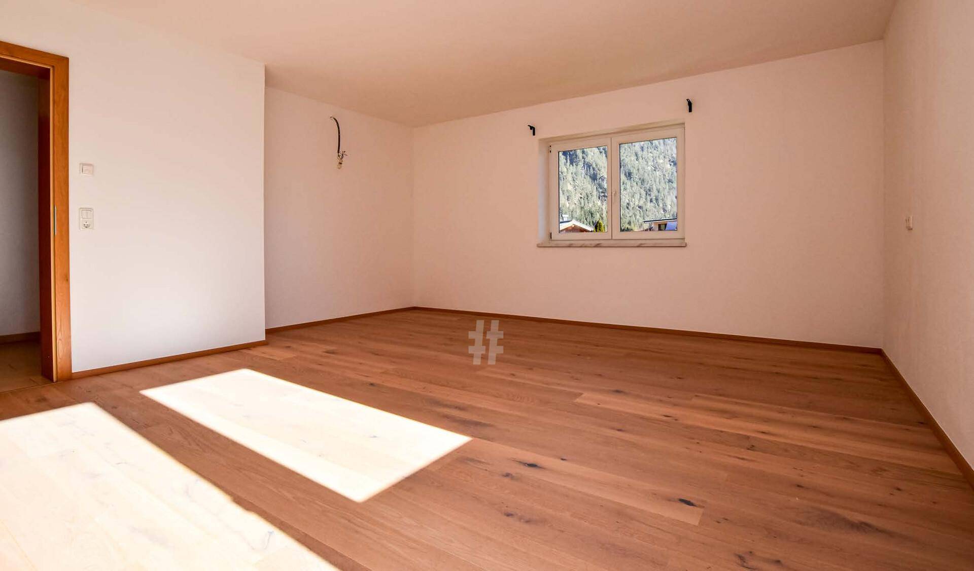 Leerer Raum mit warmem Holzboden und einem Fenster, das einen schönen Bergblick bietet.