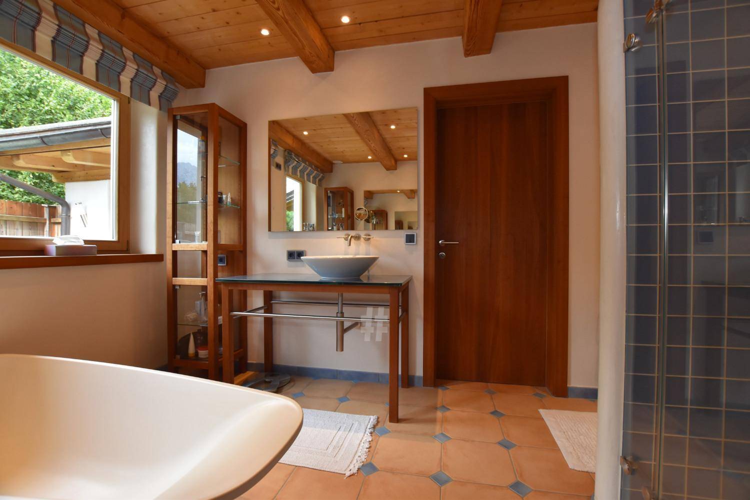 Badezimmer mit freistehender Badewanne, modernem Waschbecken und Holzbalkendecke.