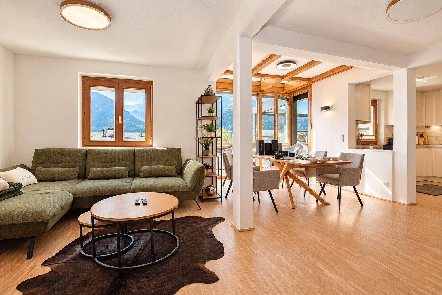 Gemütliches Wohnzimmer mit grünem Sofa, Holzboden und weitem Blick ins Grüne.