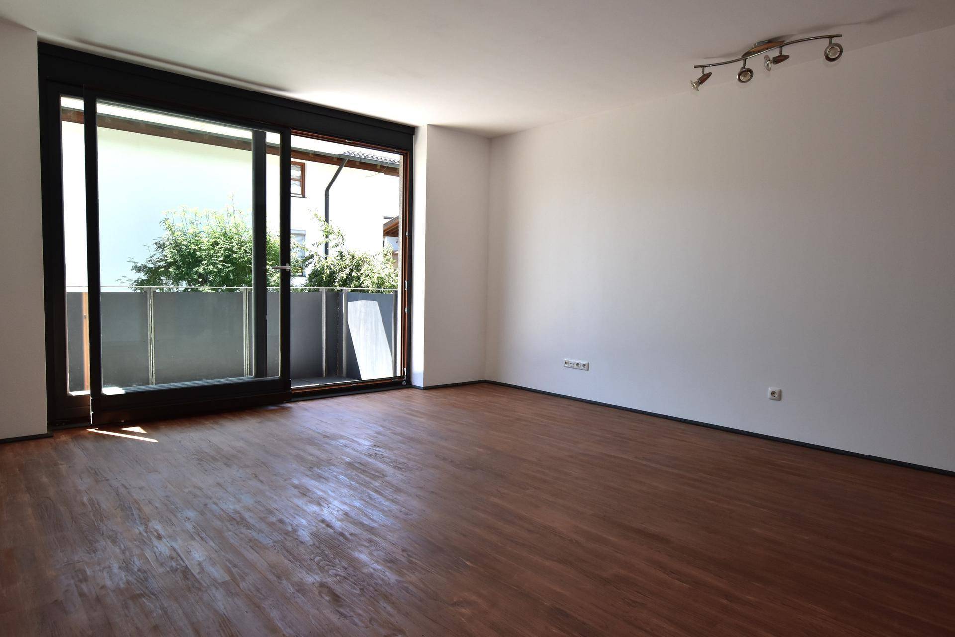 Heller Wohnraum mit großzügigem Balkonzugang durch Schiebetüren und Laminatboden.