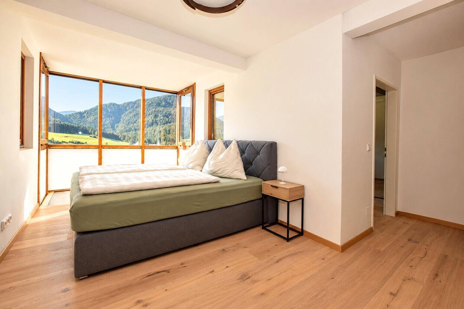 Schlafzimmer mit Doppelbett, Holzboden und großen Fenstern mit Bergblick.