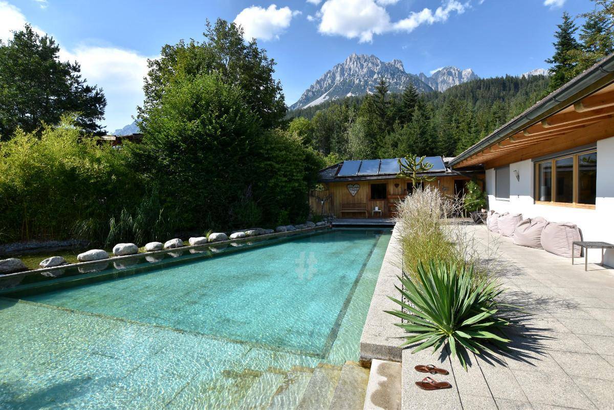 Großer Außenpool mit gepflasterter Terrasse und Bergblick im Hintergrund.