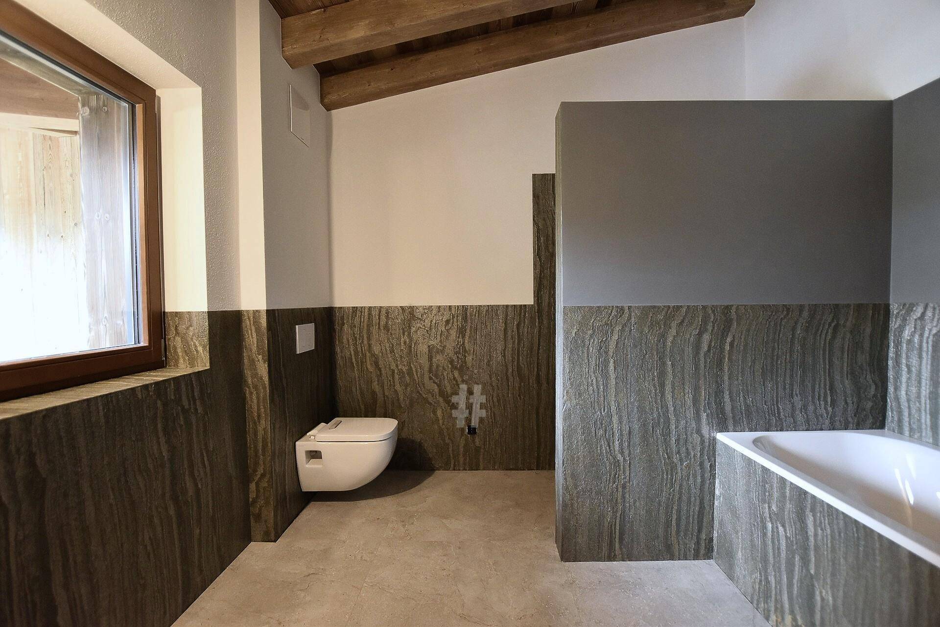 Modernes Badezimmer in Bauphase mit Wand-WC, Badewanne und eleganten Steinoptik-Fliesen.