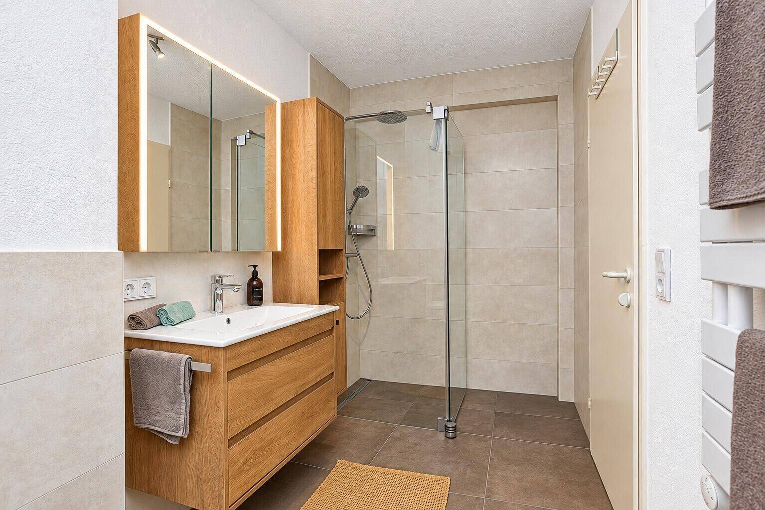 Helles Badezimmer mit Holzmöbeln, großer begehbarer Dusche und modernen Fliesen.