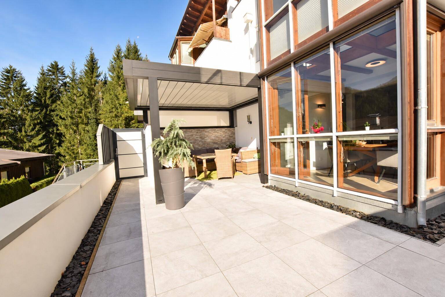 Geräumige Terrasse mit Fliesenboden, überdachtem Sitzbereich und angrenzendem Wintergarten.