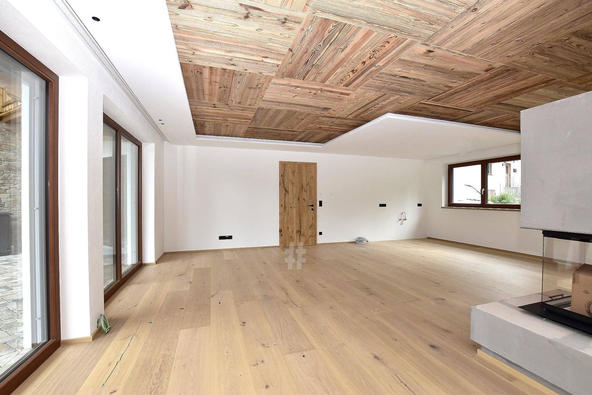Heller Wohnbereich mit Holzboden, Holzbalkendecke und modernem Kamin, bereit für die Einrichtung.