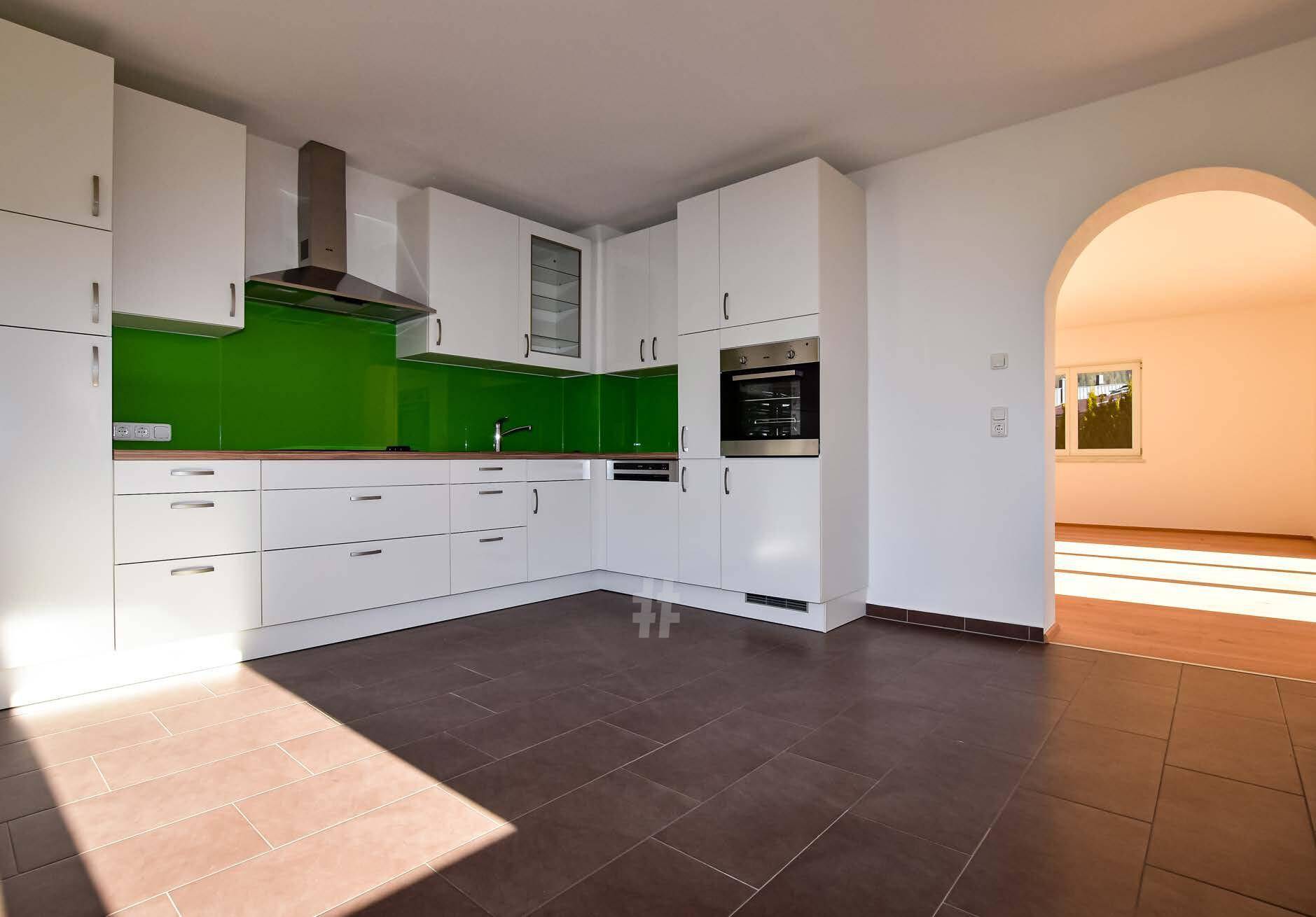 Moderne Einbauküche mit weißen Schränken, grüner Rückwand und dunklen Fliesenböden.