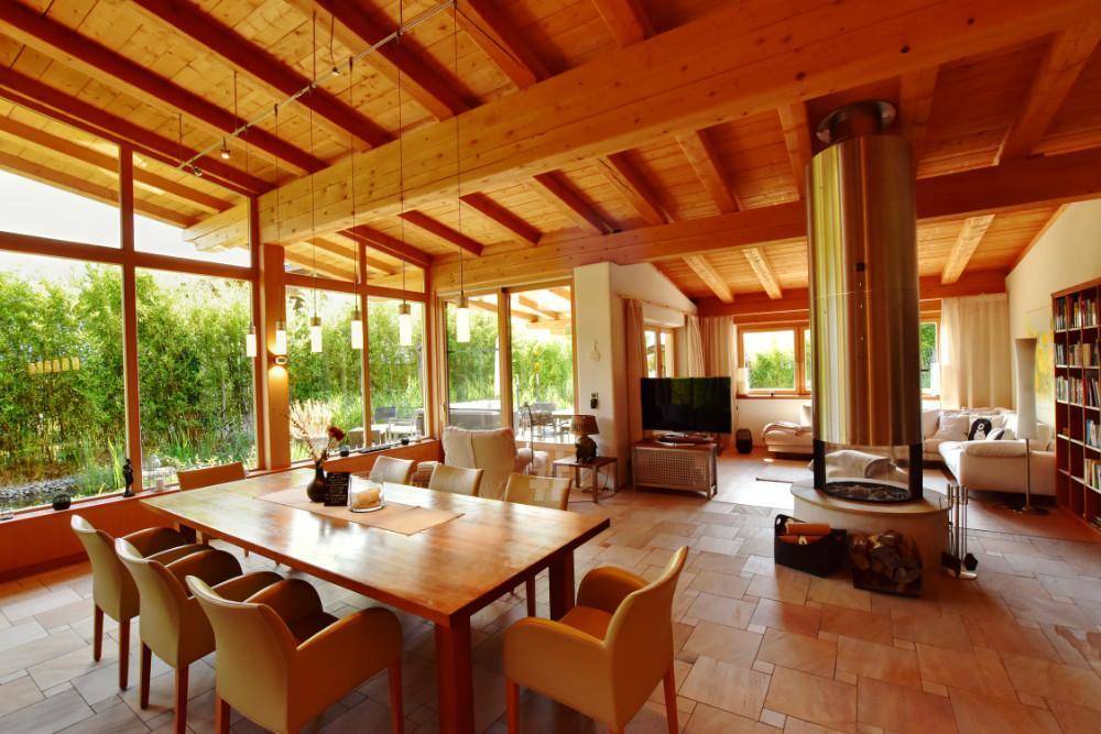 Großzügiger Wohn-Essbereich mit hohen Holzdecken, Kamin und großen Fensterfronten zum Garten.
