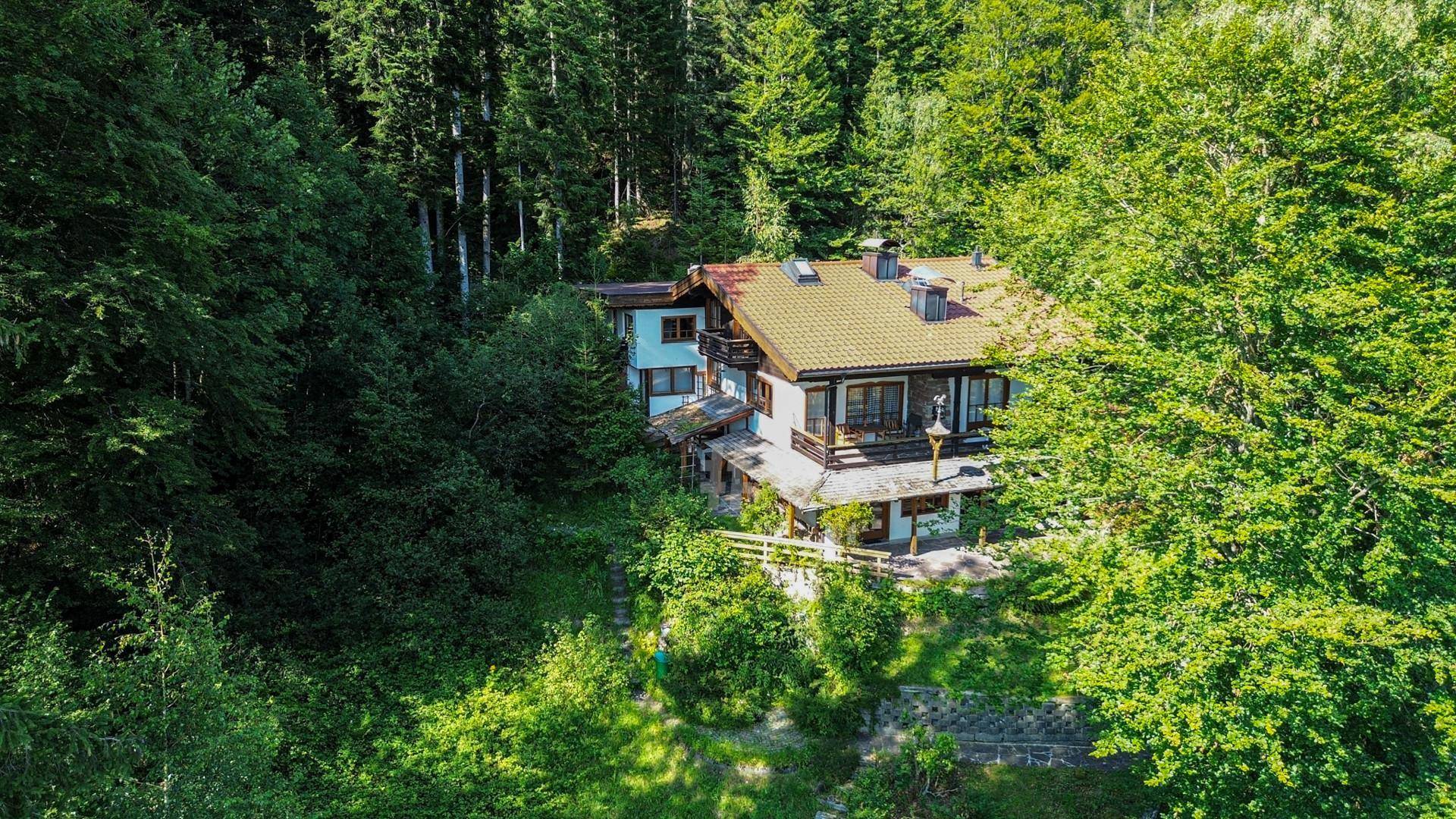 Luftaufnahme eines traditionellen Hauses, eingebettet in dichte Wälder und üppiges Grün.