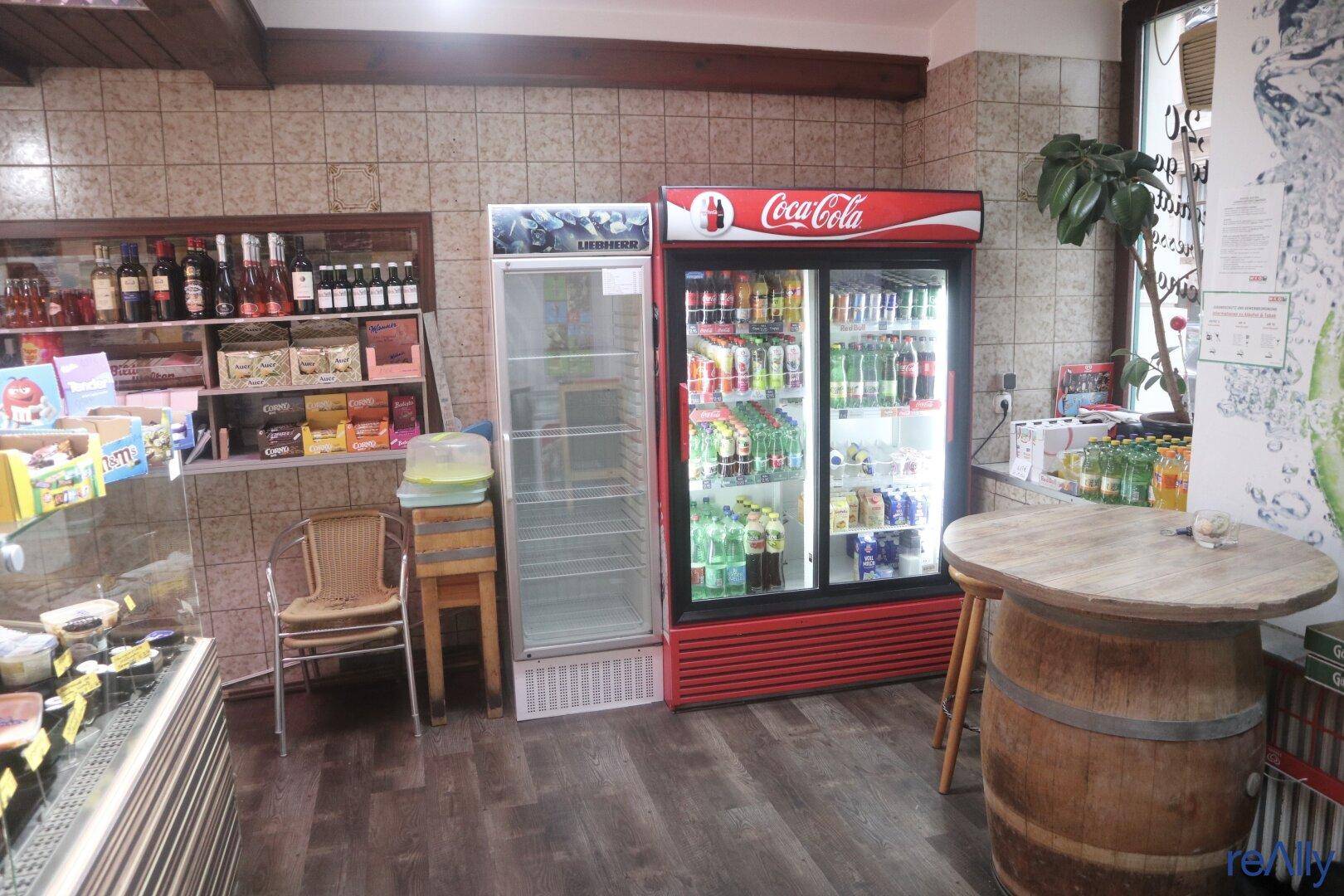 Innenansicht des Ladens mit Getränkekühlern, einer kleinen Sitzecke und der Verkaufstheke im Hintergrund.