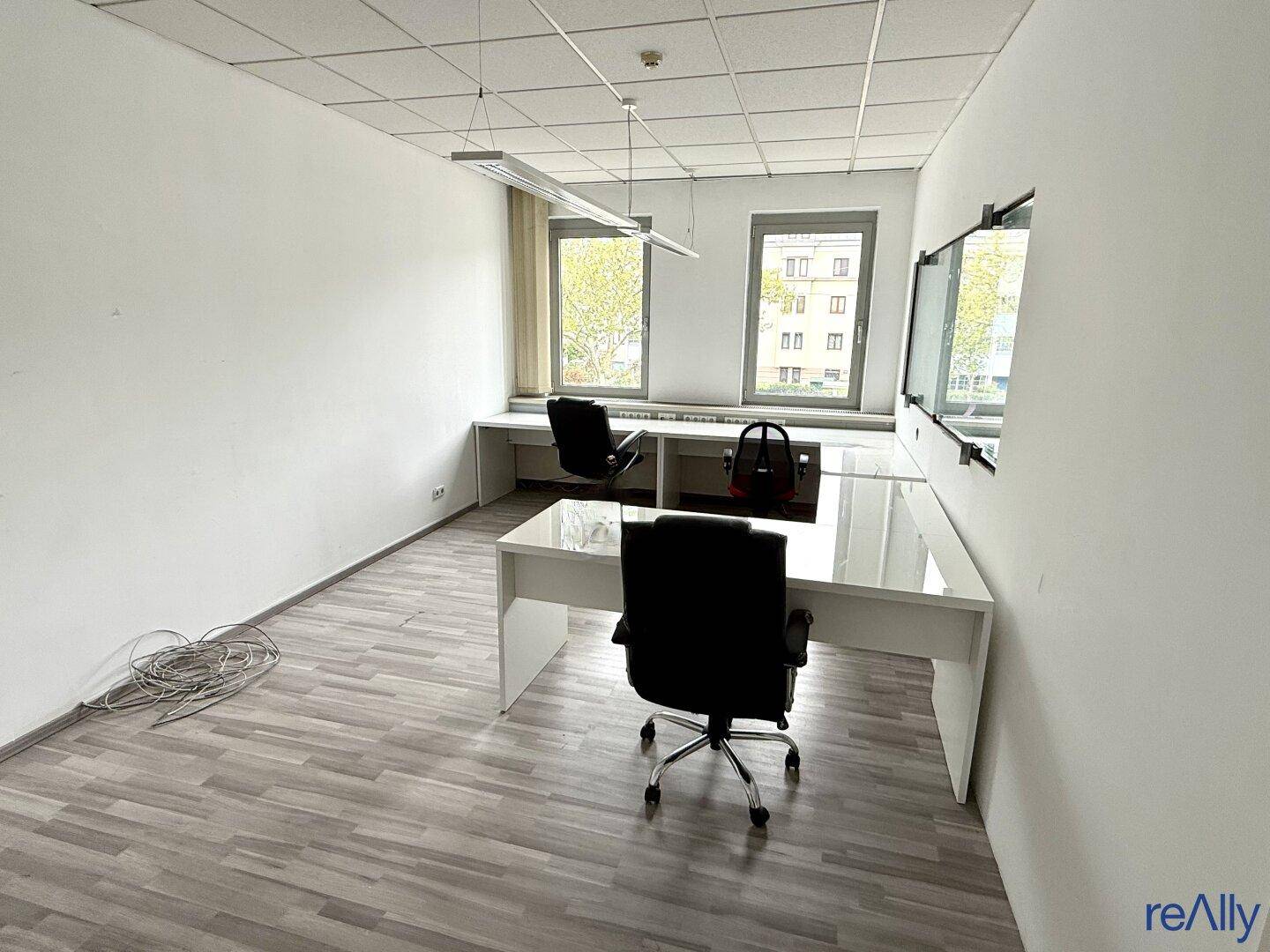 Büro mit zwei Arbeitsplätzen, hellem Laminatboden und Blick ins Grüne durch die Fenster.