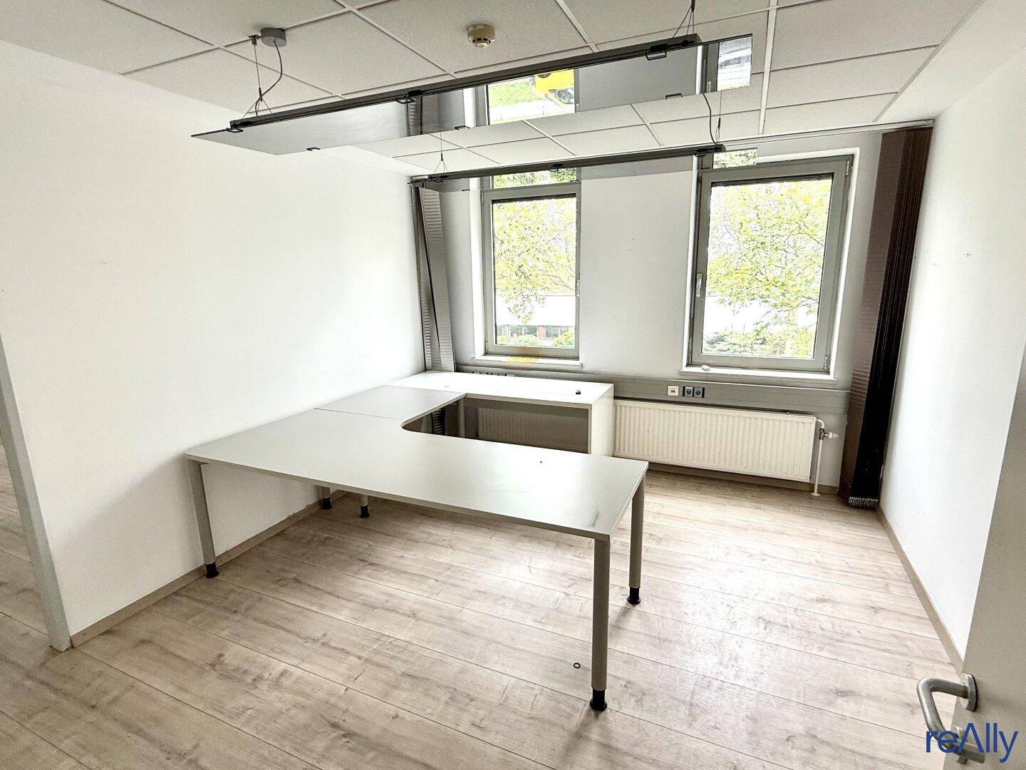Kompaktes Büro mit Eckschreibtisch, hellem Boden und Fenstern, die viel Licht hereinlassen.