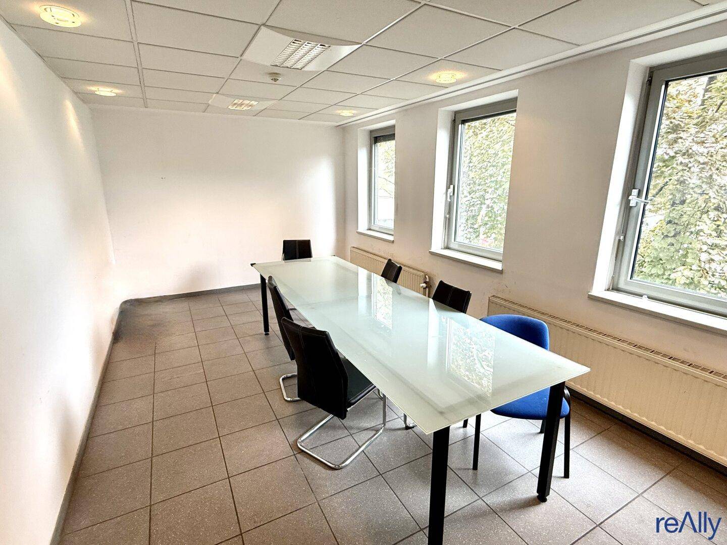 Besprechungsraum mit großem Glastisch, bequemen Stühlen und Fliesenboden.