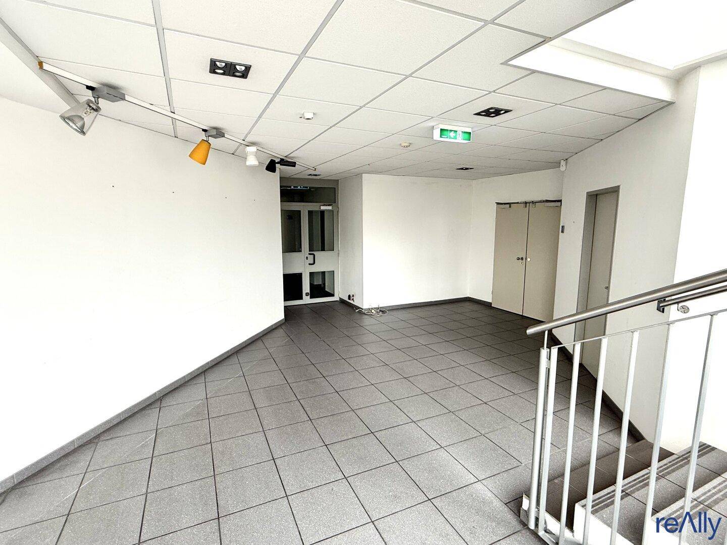 Heller Empfangsbereich mit Fliesenboden und einer Treppe, die zu den oberen Etagen führt.