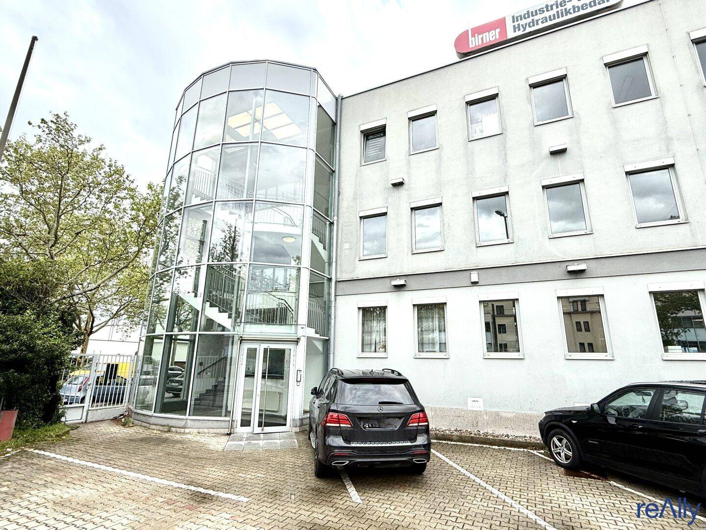 Eingangsbereich des Bürogebäudes mit markanter Glasrotunde und gepflastertem Vorplatz.