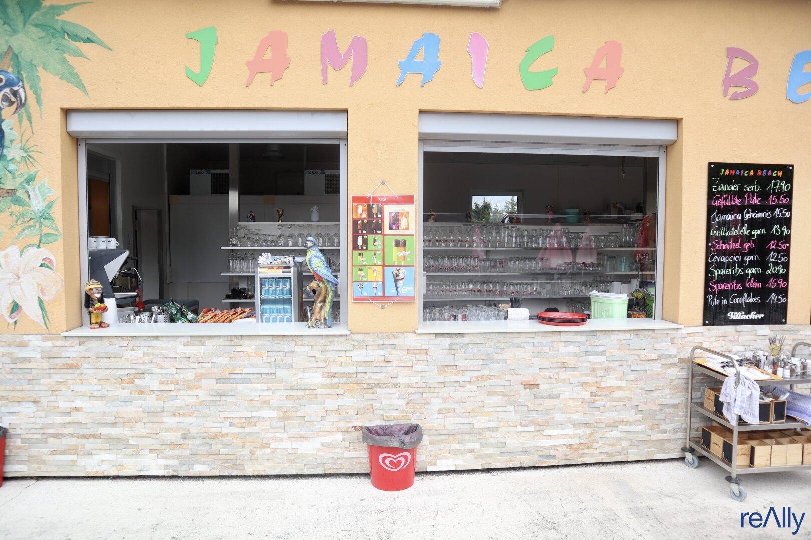 Servicefenster eines Gebäudes mit "Jamaica Beach" Beschriftung und einer Steinverkleidung an der Fassade.