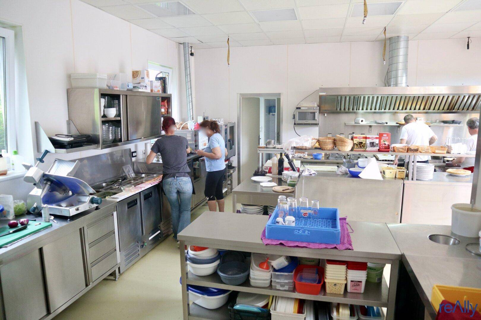 Große, professionelle Küche mit Edelstahloberflächen, Dunstabzugshauben und Personal bei der Arbeit.