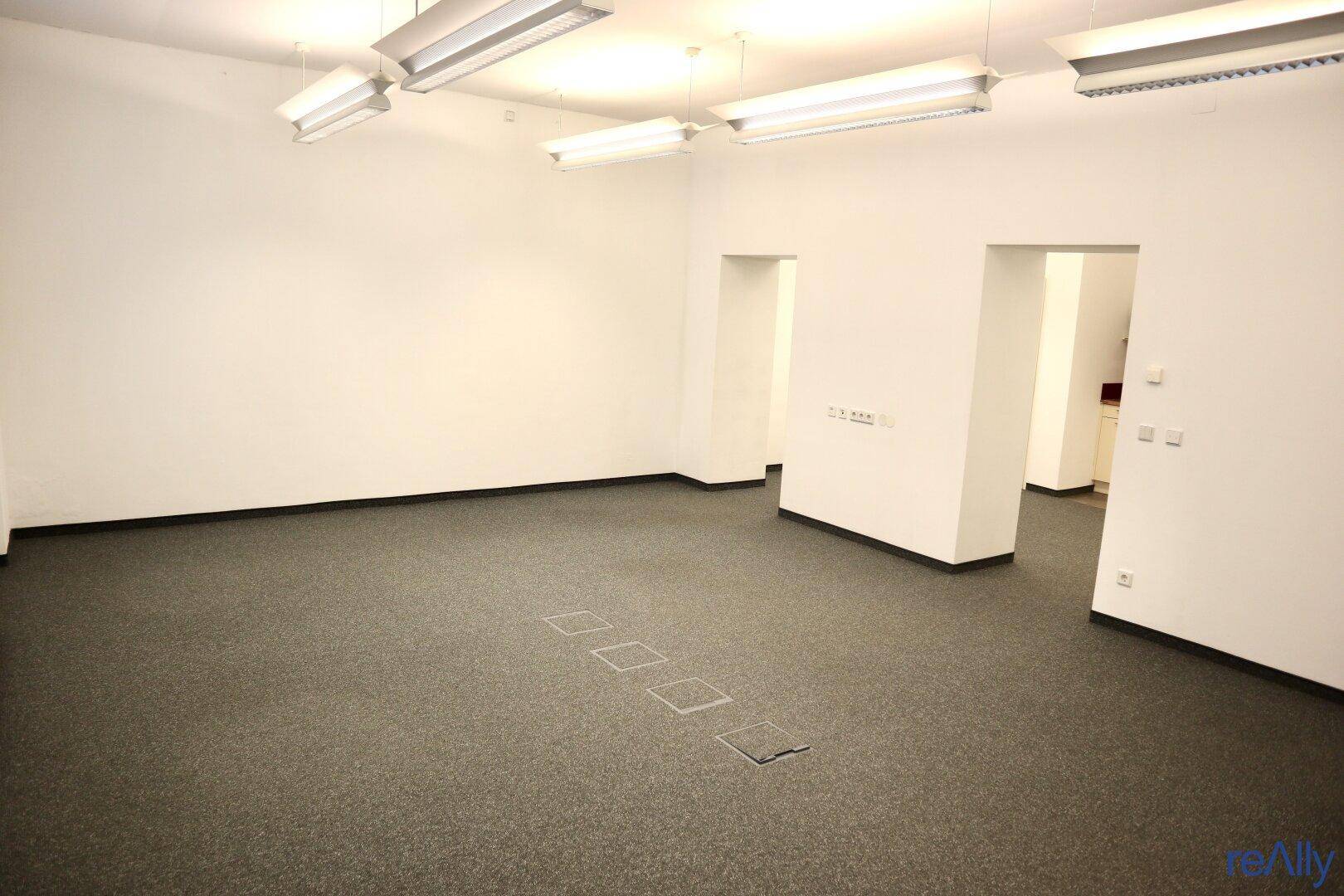 Geräumiger, leerer Büroraum mit Teppichboden und Deckenleuchten, bereit zur individuellen Gestaltung.