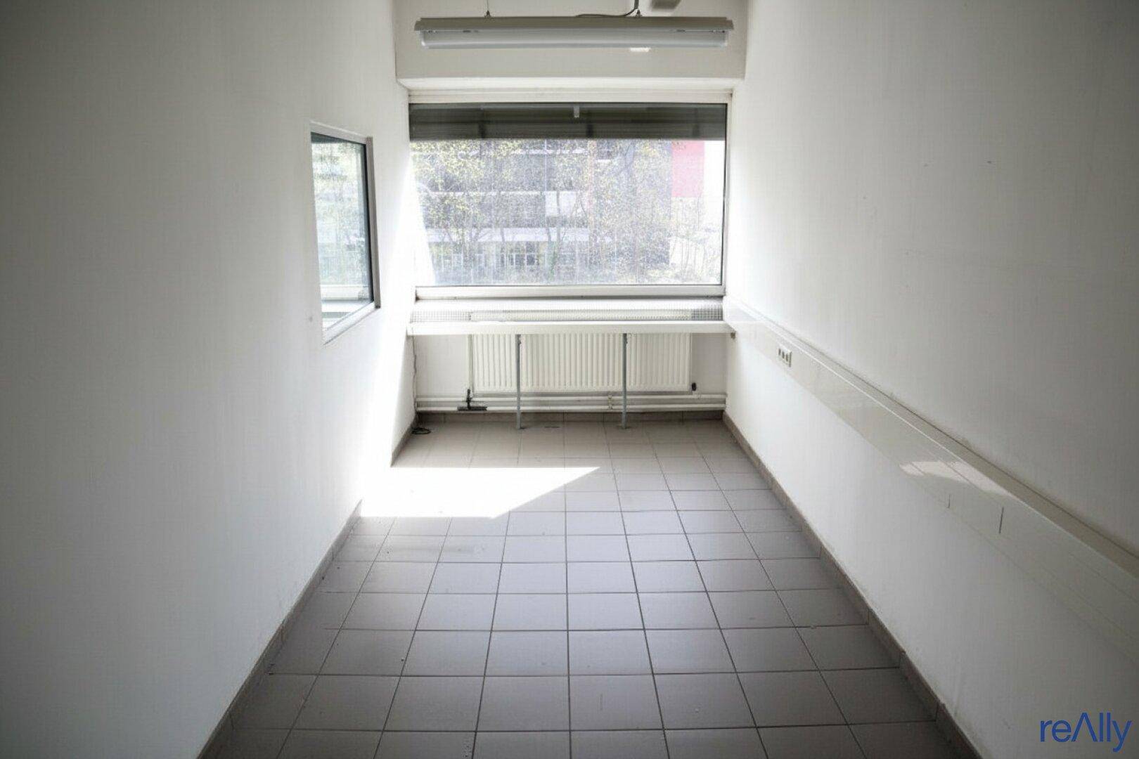 Langes, schmales Büro mit Fliesenboden, einem Fenster und natürlichem Lichteinfall.