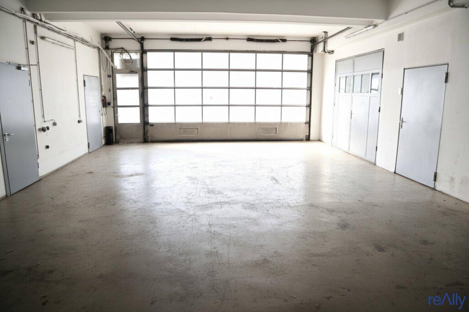 Große, leere Garage mit Betonboden und einem breiten Rolltor, das viel Licht hereinlässt.