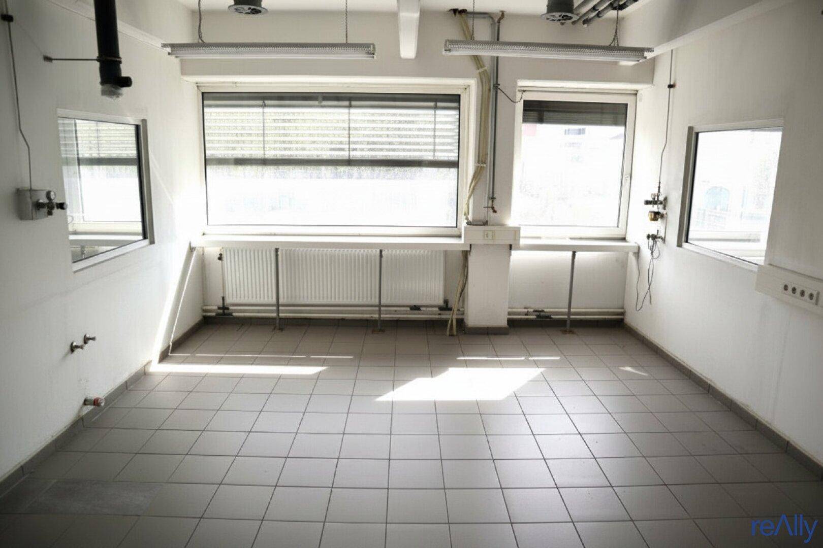 Geräumiges Büro mit Fliesenboden, großen Fenstern und viel natürlichem Licht.