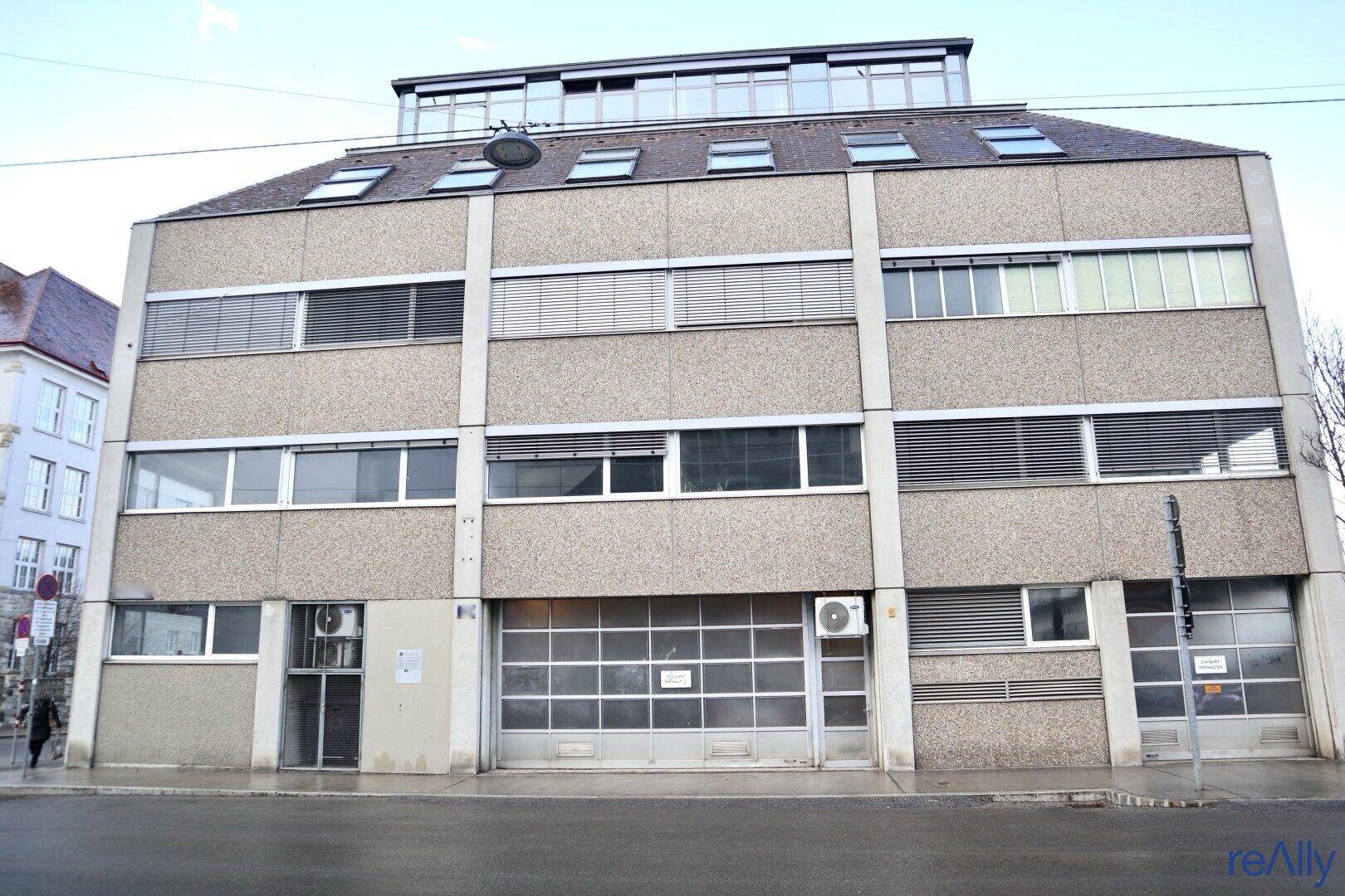 Fassade eines Geschäftsgebäudes mit mehreren Fenstern, Jalousien und Garagentoren im Erdgeschoss.