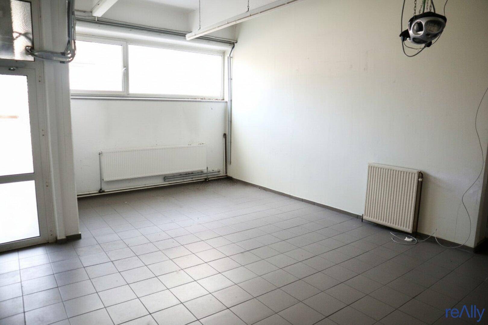 Geräumiger Büroraum mit Fliesenboden, großen Fenstern und Heizkörpern an den Wänden, hell und funktional.
