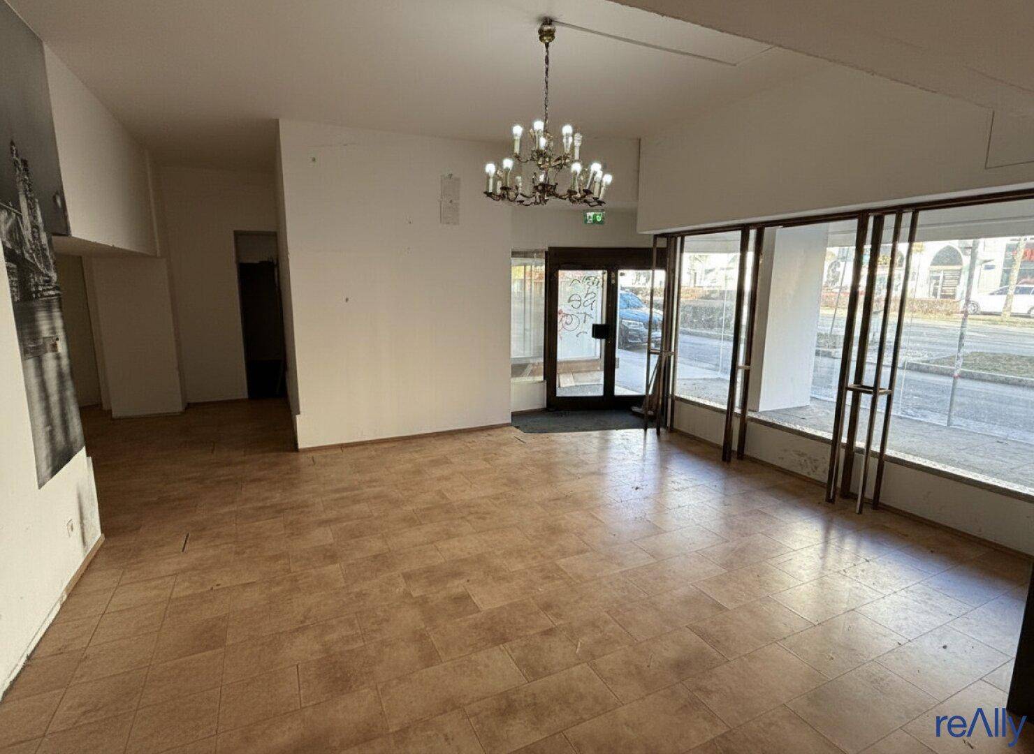 Heller Ladenraum mit Fliesenboden, großen Fenstern zur Straße und einem Eingangsbereich.
