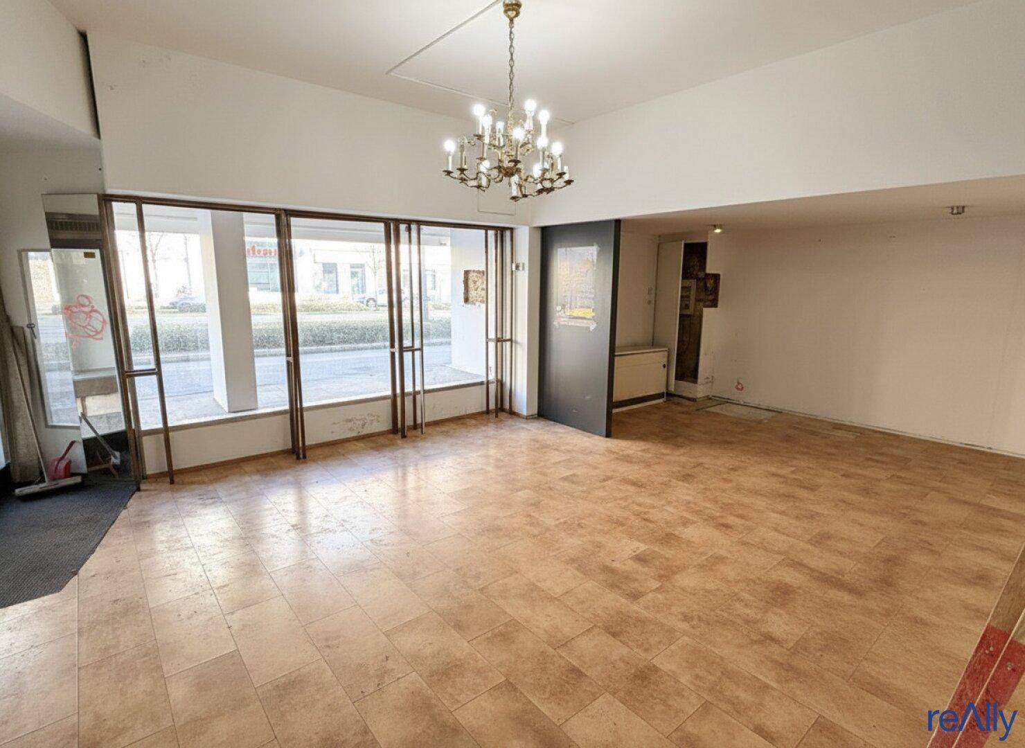 Geräumiger, leerer Ladenraum mit großen Schaufenstern und einem Kronleuchter an der Decke.