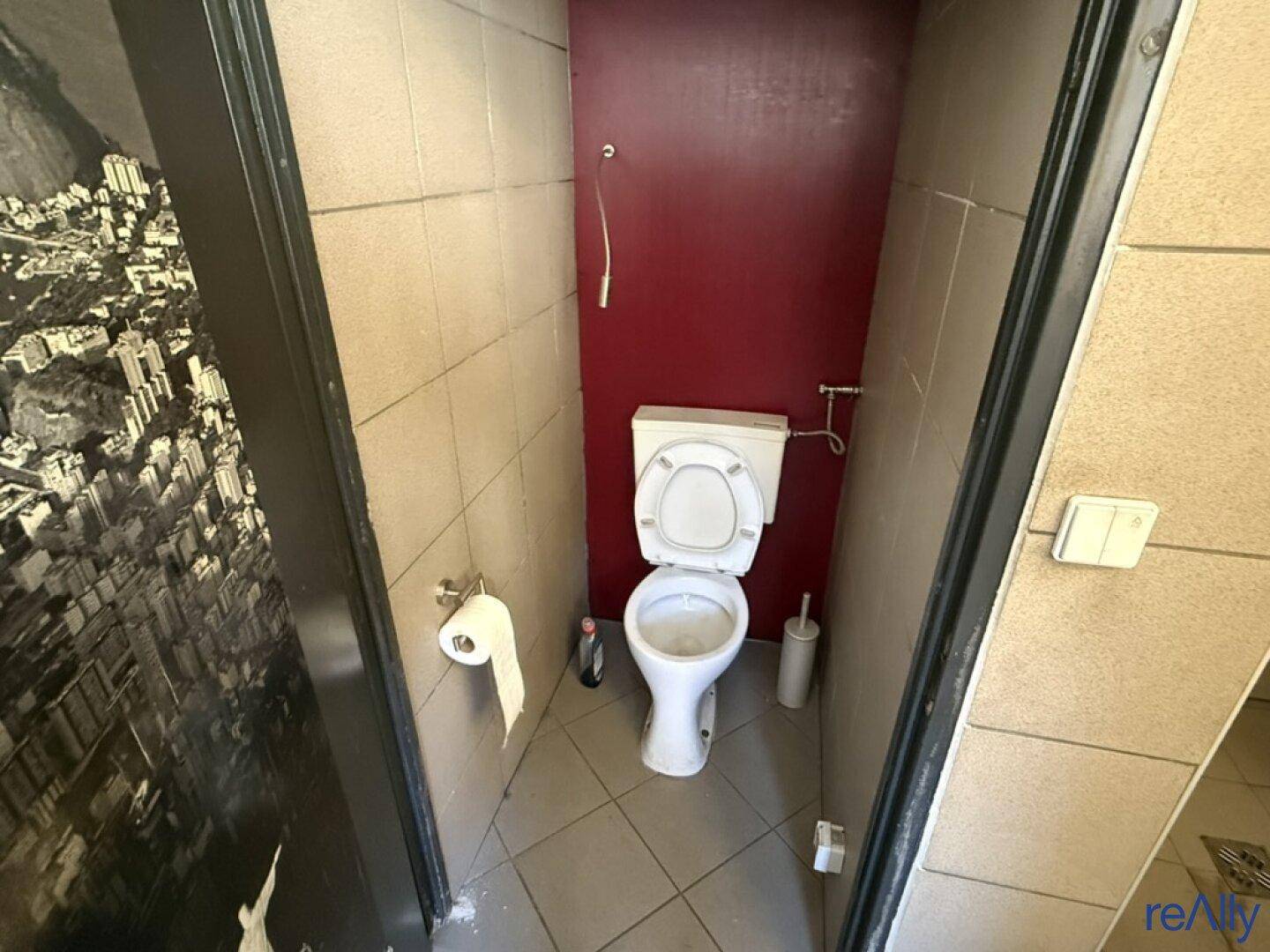 Kleine Gästetoilette mit WC und Fliesen an Wänden und Boden, akzentuiert durch eine rote Wand.