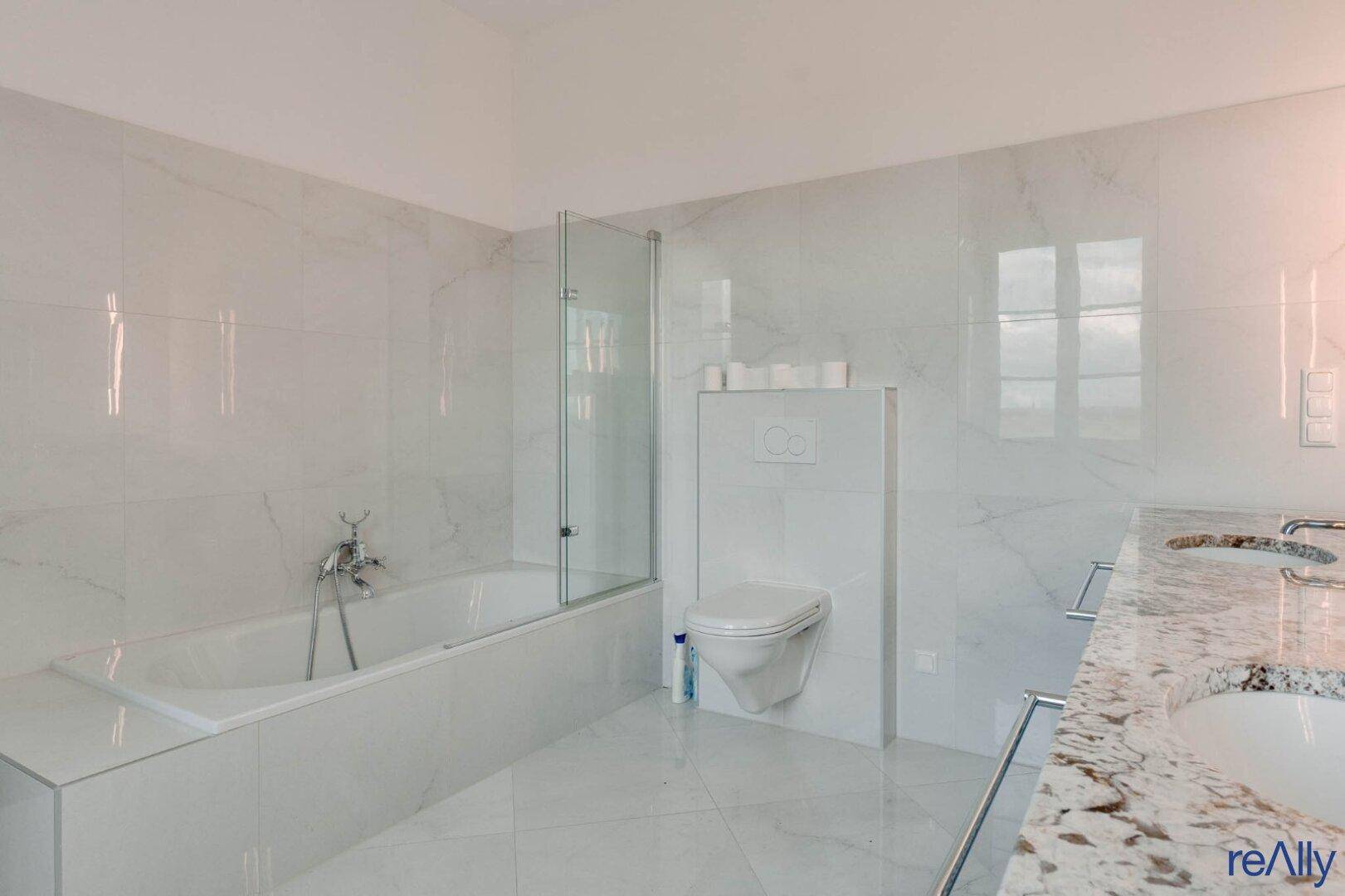 Modernes Badezimmer mit weißen Marmorfliesen, Badewanne und Doppelwaschbecken.