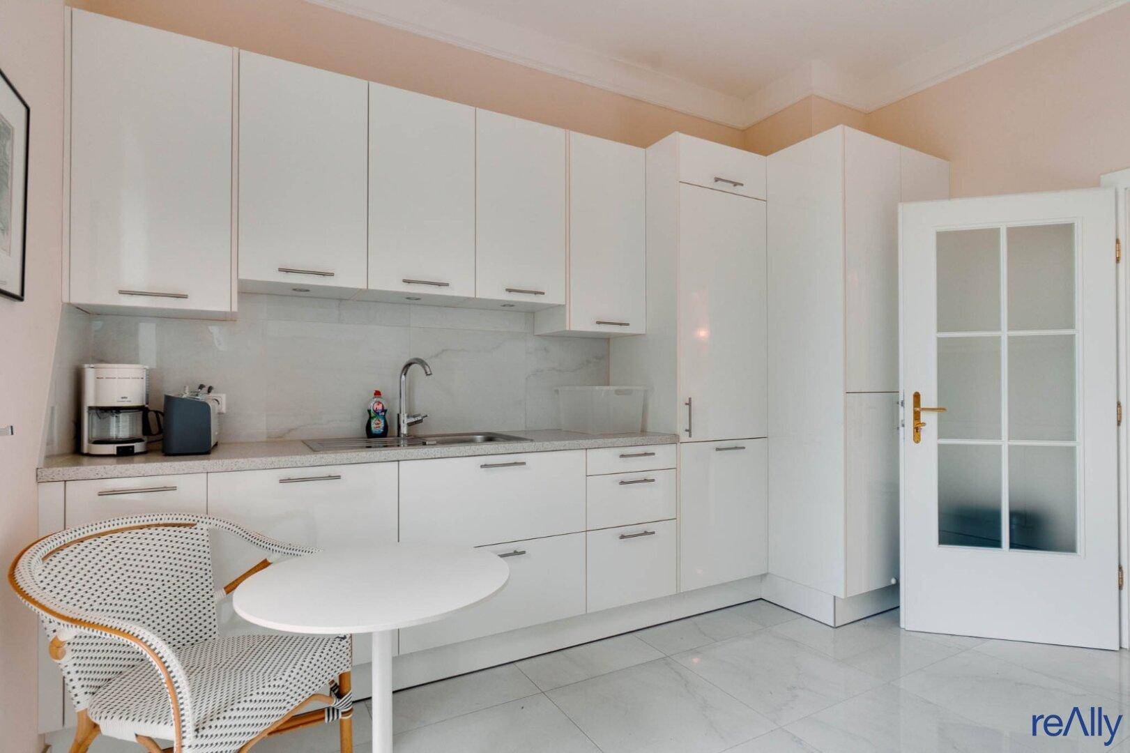 Helle Einbauküche mit weißen Hochglanzschränken, Essbereich und Zugang nach draußen.