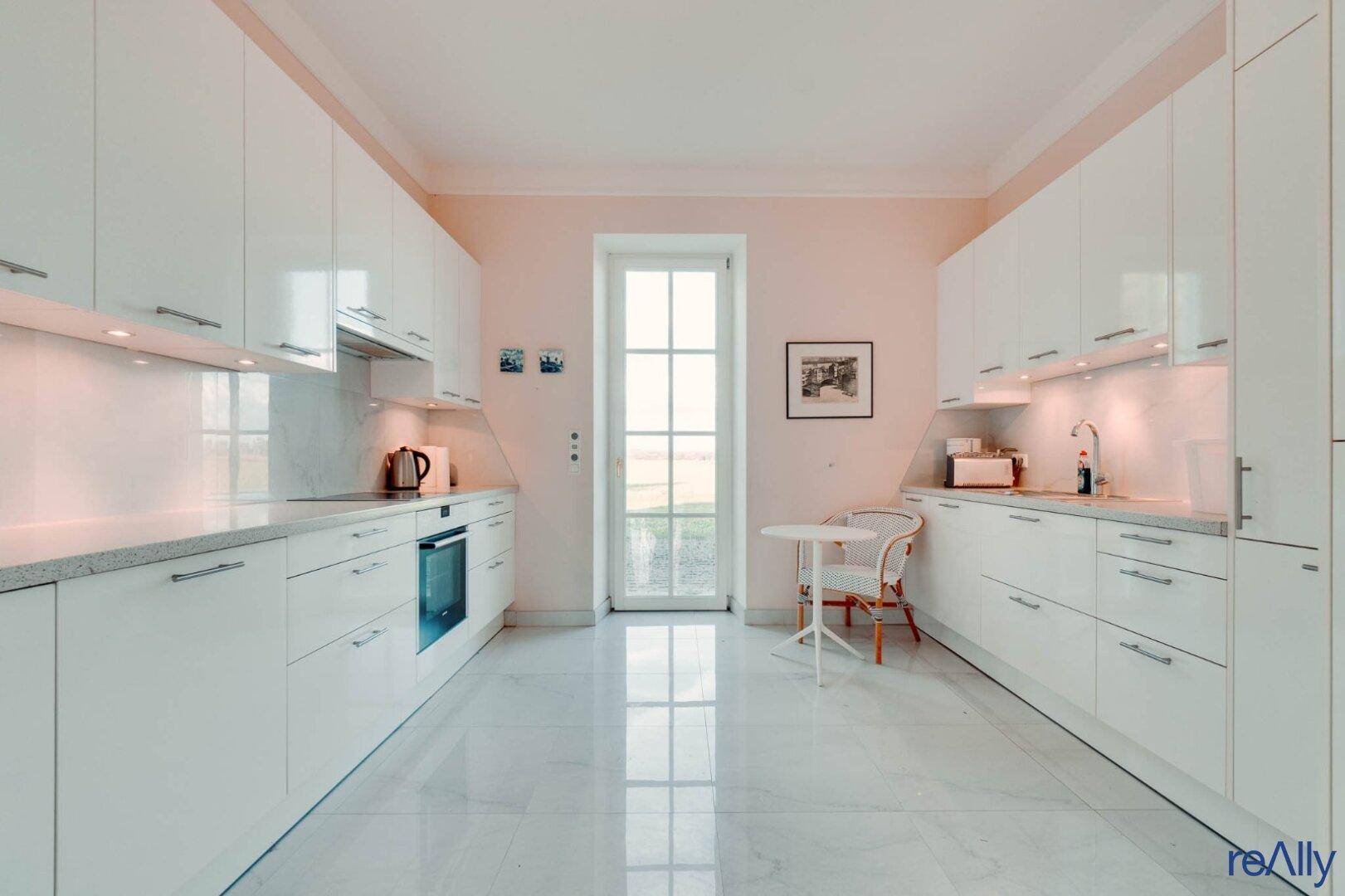 Geräumige Küche mit weißen Schränken, modernen Geräten und Zugang zum Garten.