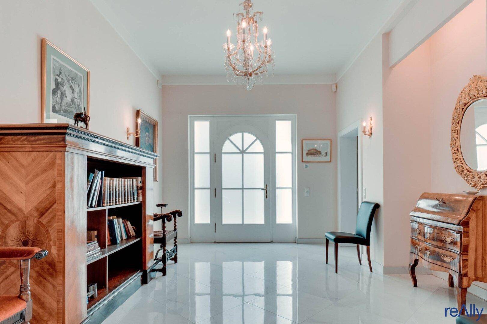 Eleganter Eingangsbereich mit glänzendem Fliesenboden, Kronleuchter und antiken Möbeln.