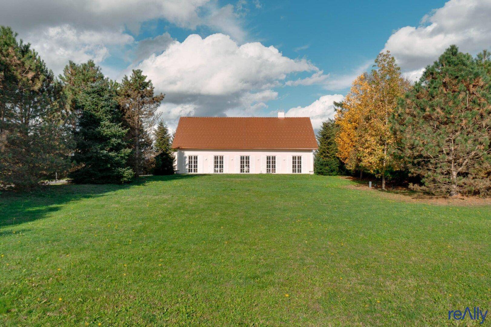 Elegantes Landhaus mit rotem Ziegeldach, umgeben von einer weitläufigen grünen Wiese.