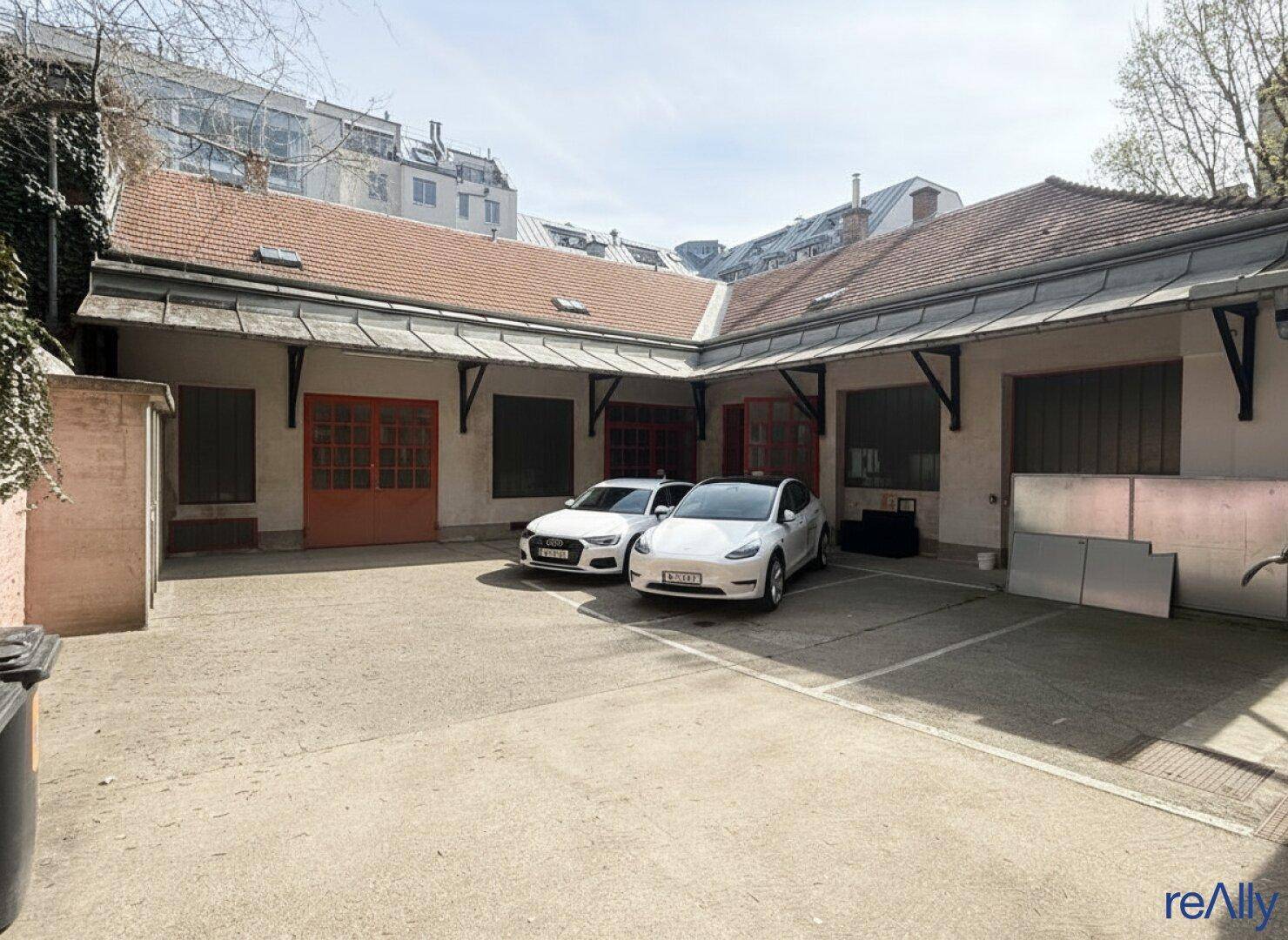 Geräumiger Innenhof mit Parkplätzen und einem Gebäude mit roten Türen und Ziegeldach.