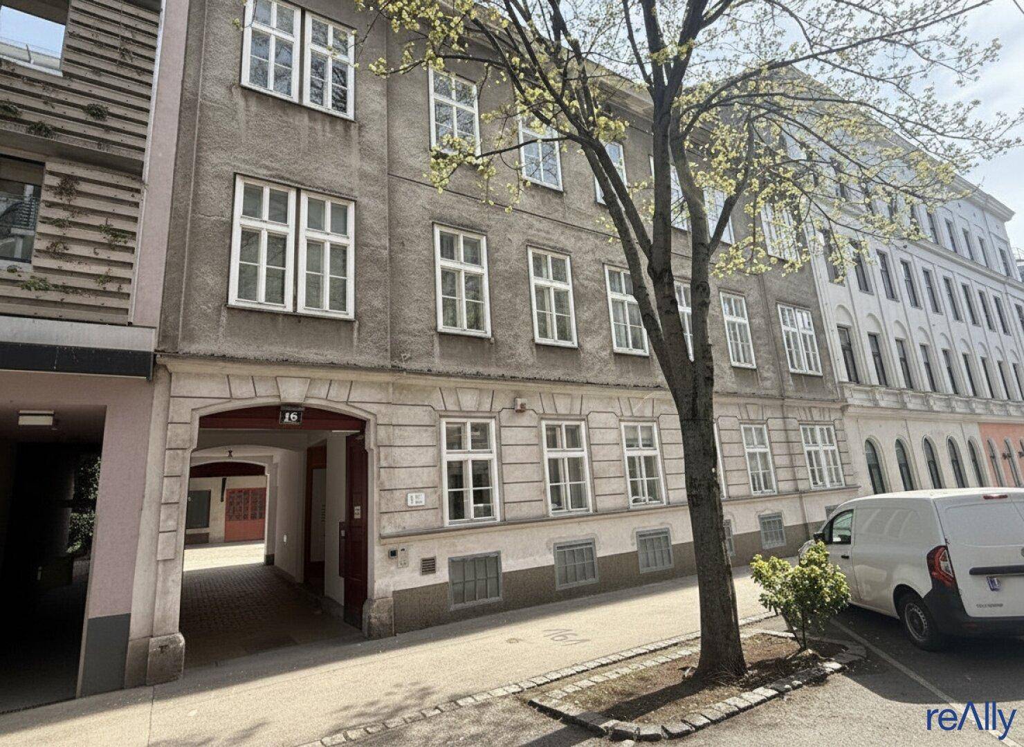 Historisches Gebäude mit klassischer Fassade, vielen Fenstern und einem Durchgang zum Innenhof.