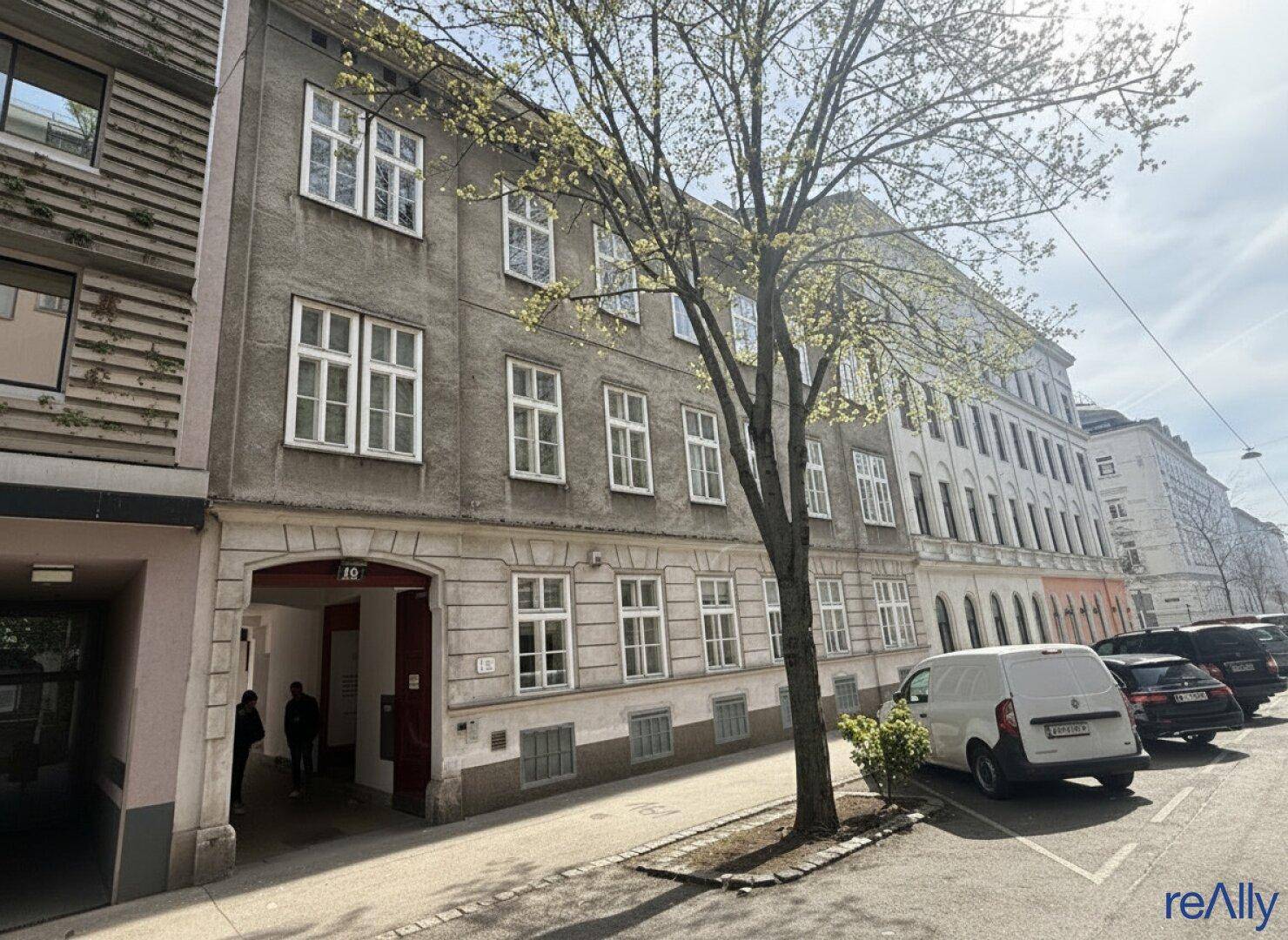 Historisches Gebäude mit klassischer Fassade, vielen Fenstern und einem Durchgang zum Innenhof.