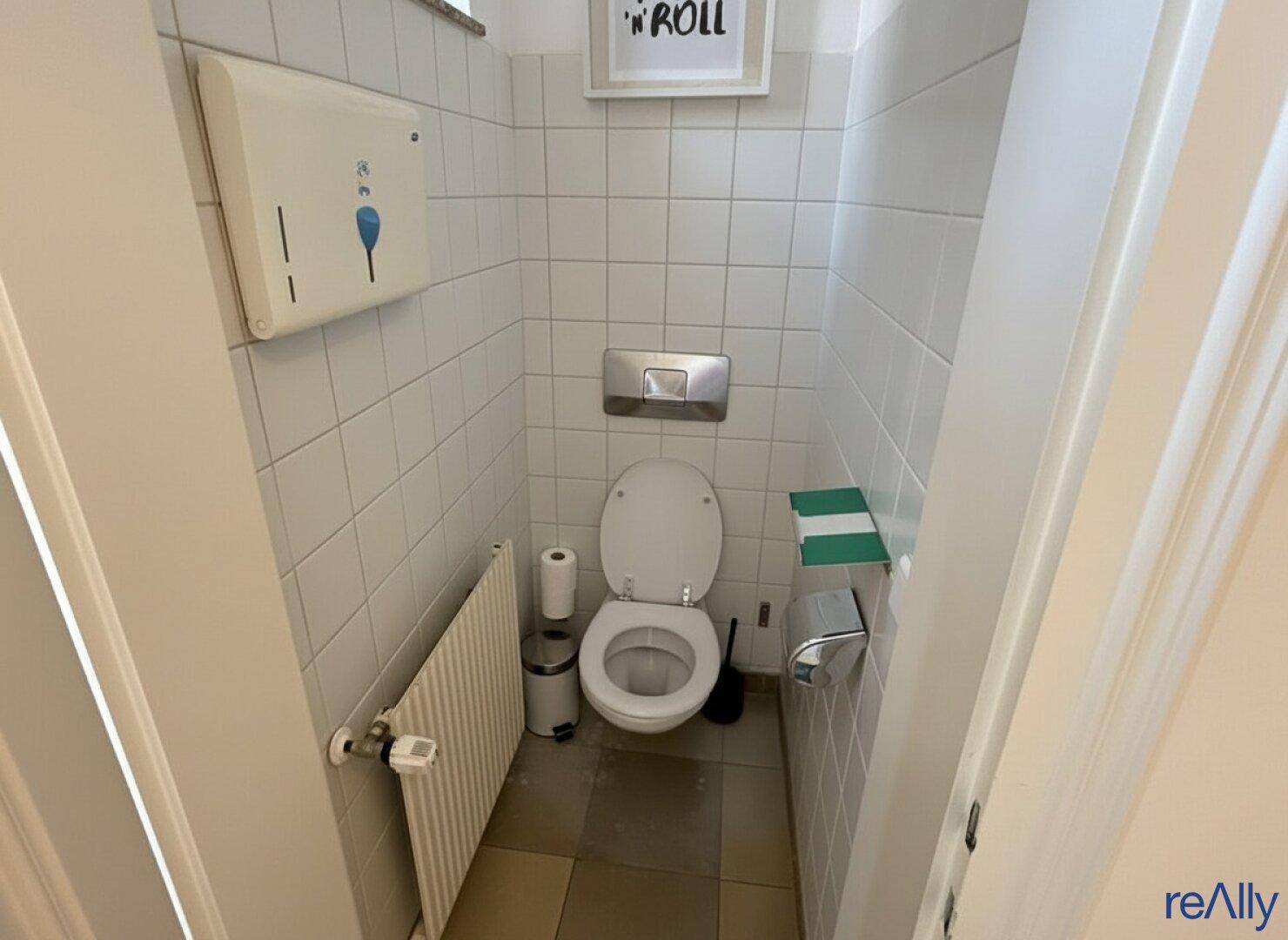 Kleines Badezimmer mit weißen Fliesen, Toilette und Heizkörper, sauber und funktional.