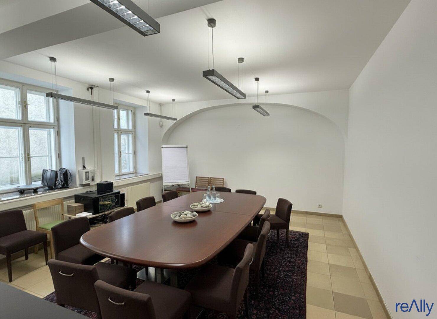 Großer Konferenzraum mit langem Holztisch, bequemen Stühlen und gewölbter Decke, ideal für Besprechungen.