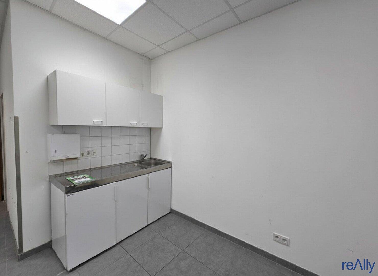 Kleine Teeküche mit weißen Unterschränken, Spülbecken und Fliesenrückwand.
