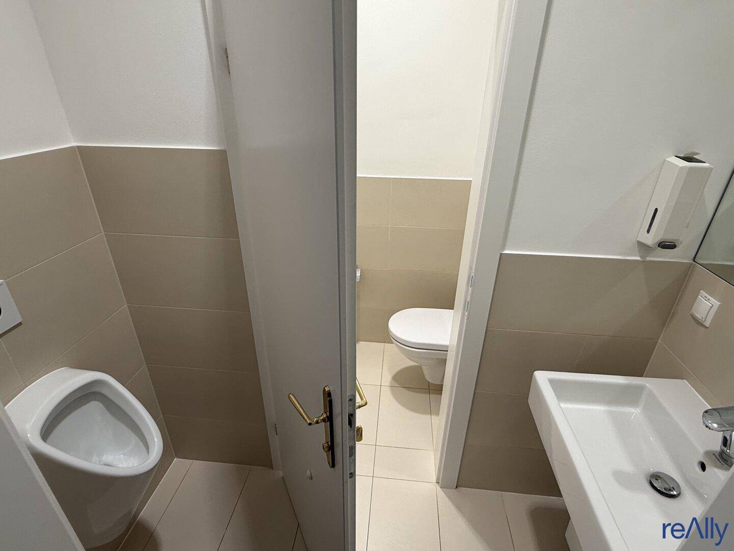 Zwei separate Toilettenräume mit Urinal, Waschbecken und hellen Fliesen, ideal für Büronutzung.