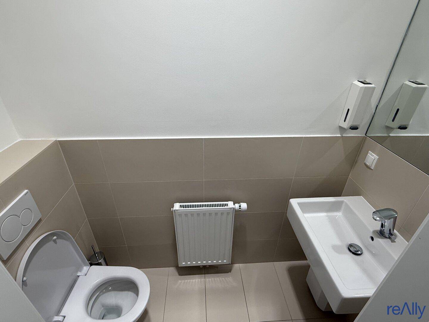 Saubere Gästetoilette mit Wand-WC, Waschbecken und Heizkörper, ausgestattet mit hellen Fliesen.